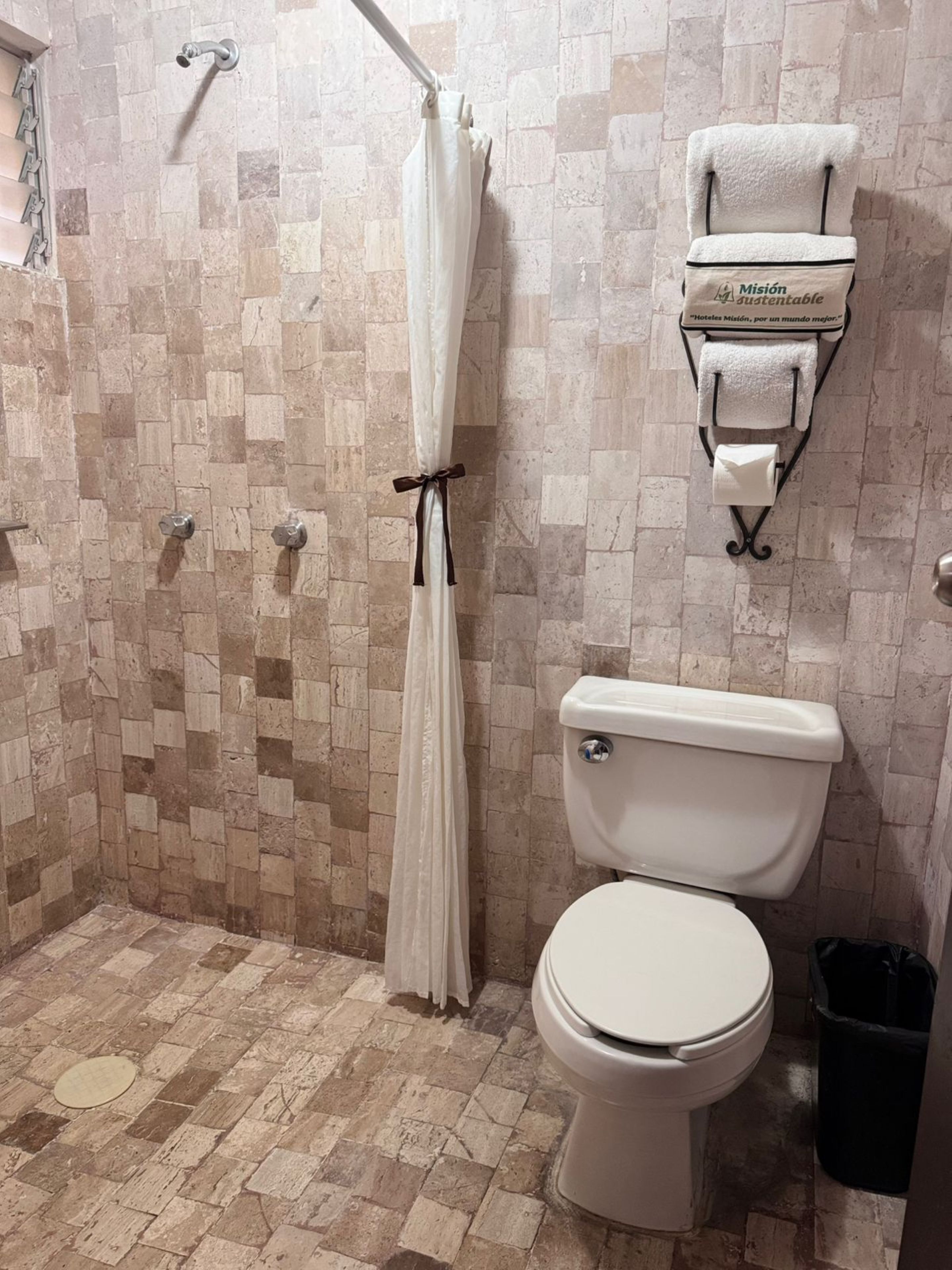 Un baño con pared de ducha azulejada, un inodoro y un perchero con una toalla.