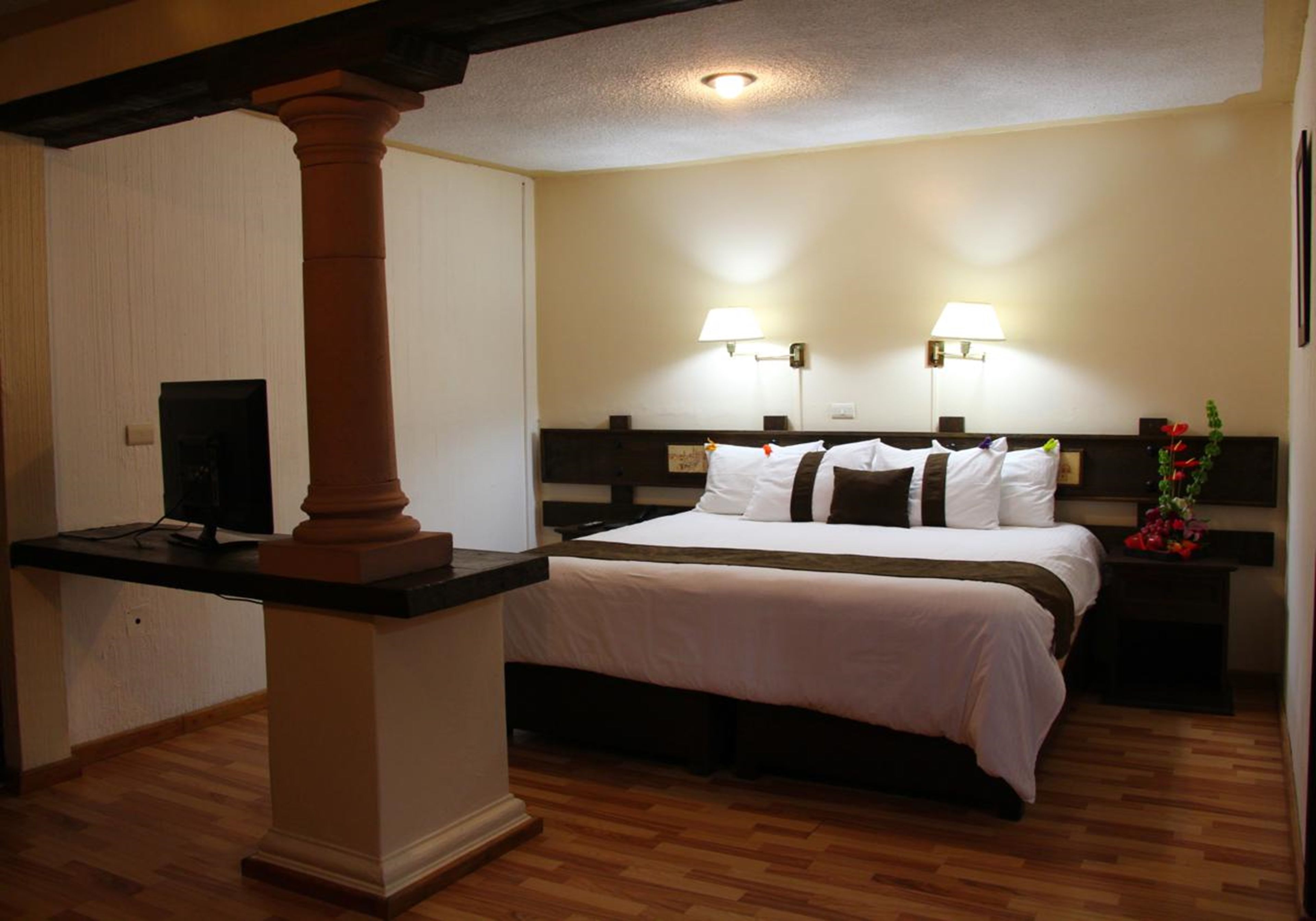 Una habitación de hotel con una cama grande, dos lámparas de noche, una mesita de noche de madera y un televisor sobre un mueble.