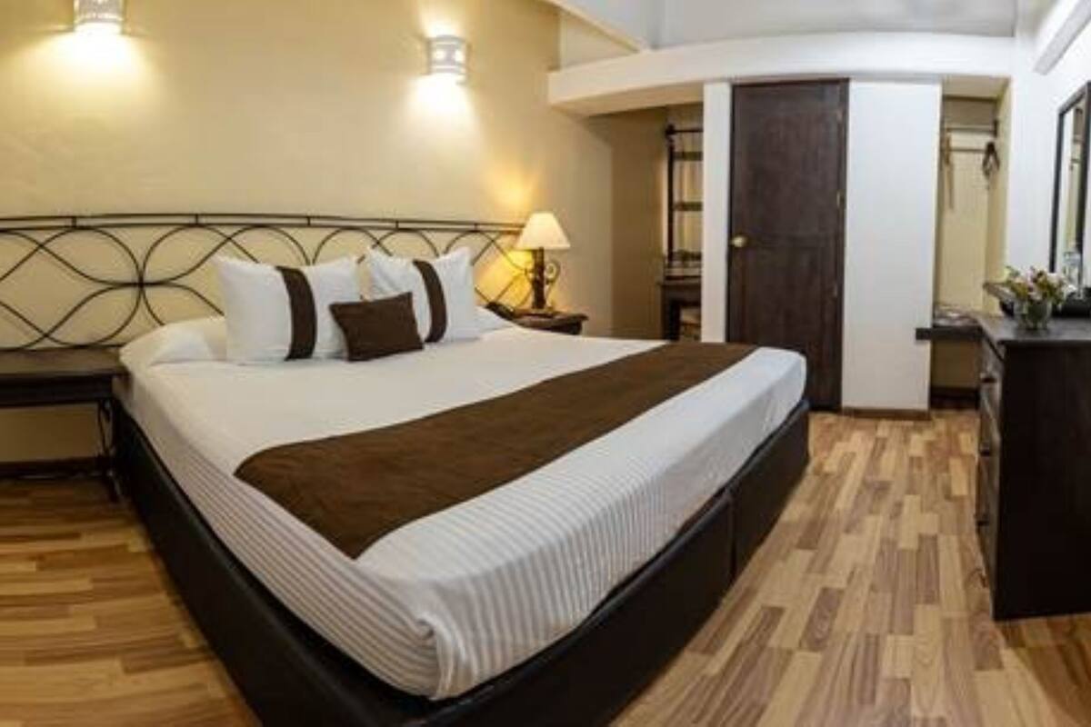 A bedroom with a large bed, a nightstand, a lamp, and a wooden floor.