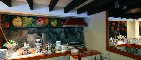 A breakfast buffet area with a stone wall and fruit-themed mural, wooden counter, and metal chairs.