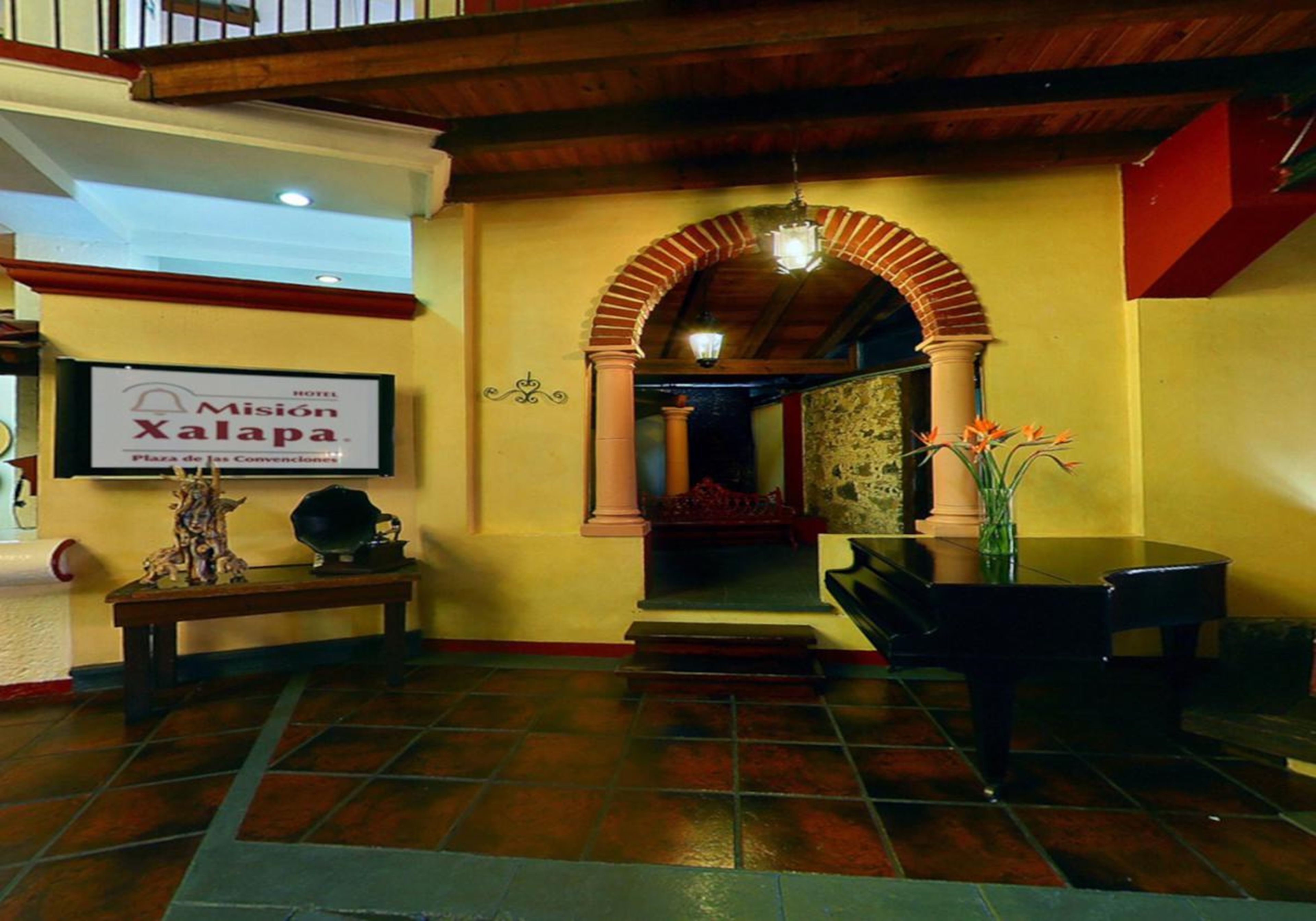 Een hotellobby met een betegelde vloer, een piano, een bank en een bord met 'Misión Xalapa'.