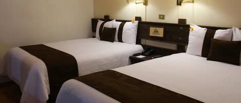 Habitación de hotel con dos camas, cada una con ropa blanca y cabeceros marrones. Hay dos lámparas de pared a cada lado de las camas.