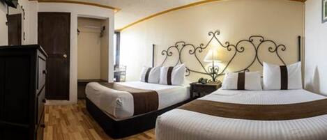 A hotel room with two beds, a wooden floor, a dark wardrobe, and a decorative headboard.