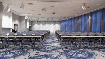 Un salón de conferencias con filas de mesas y sillas, una alfombra estampada y una pantalla de proyector.