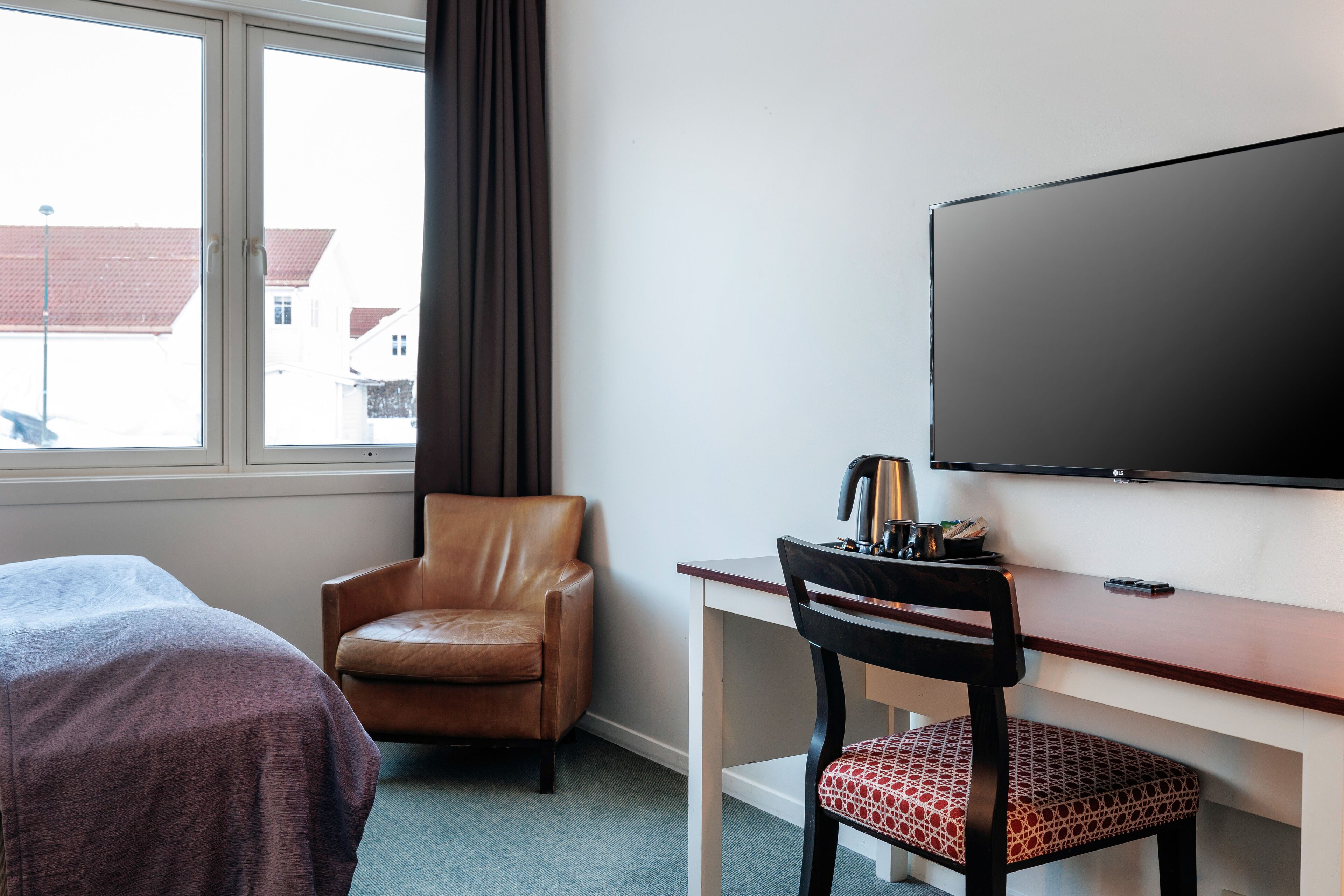 A hotel room with a bed, a desk with a chair, a television, and a window with curtains.