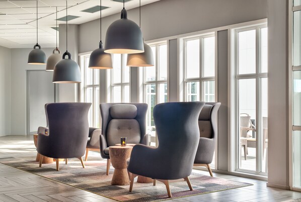 Un interior moderno con ventanas amplias, sillas de tonos oscuros e iluminación colgante.
