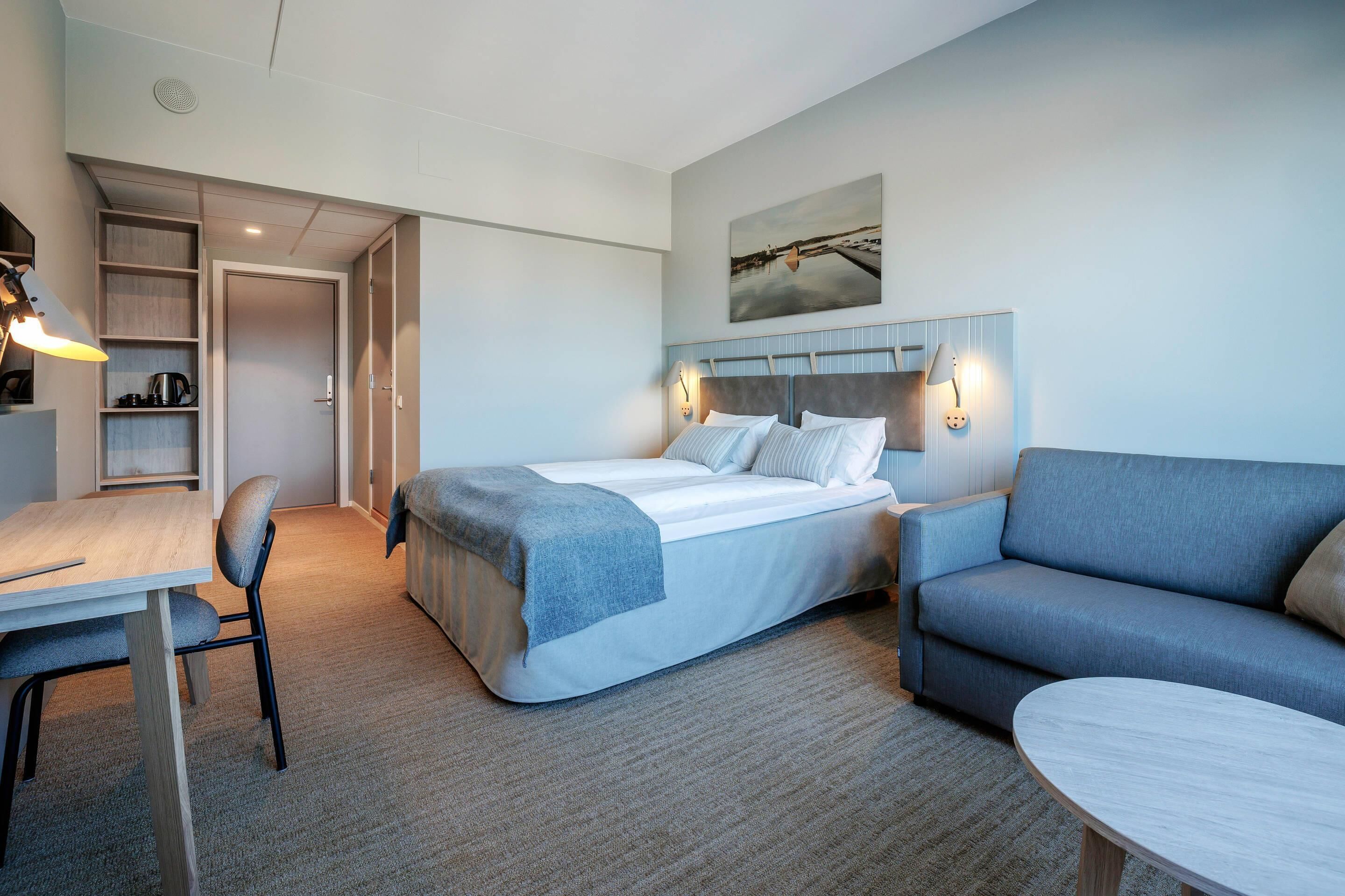 A hotel room with a bed, a desk, a chair, a sofa, and a small table.