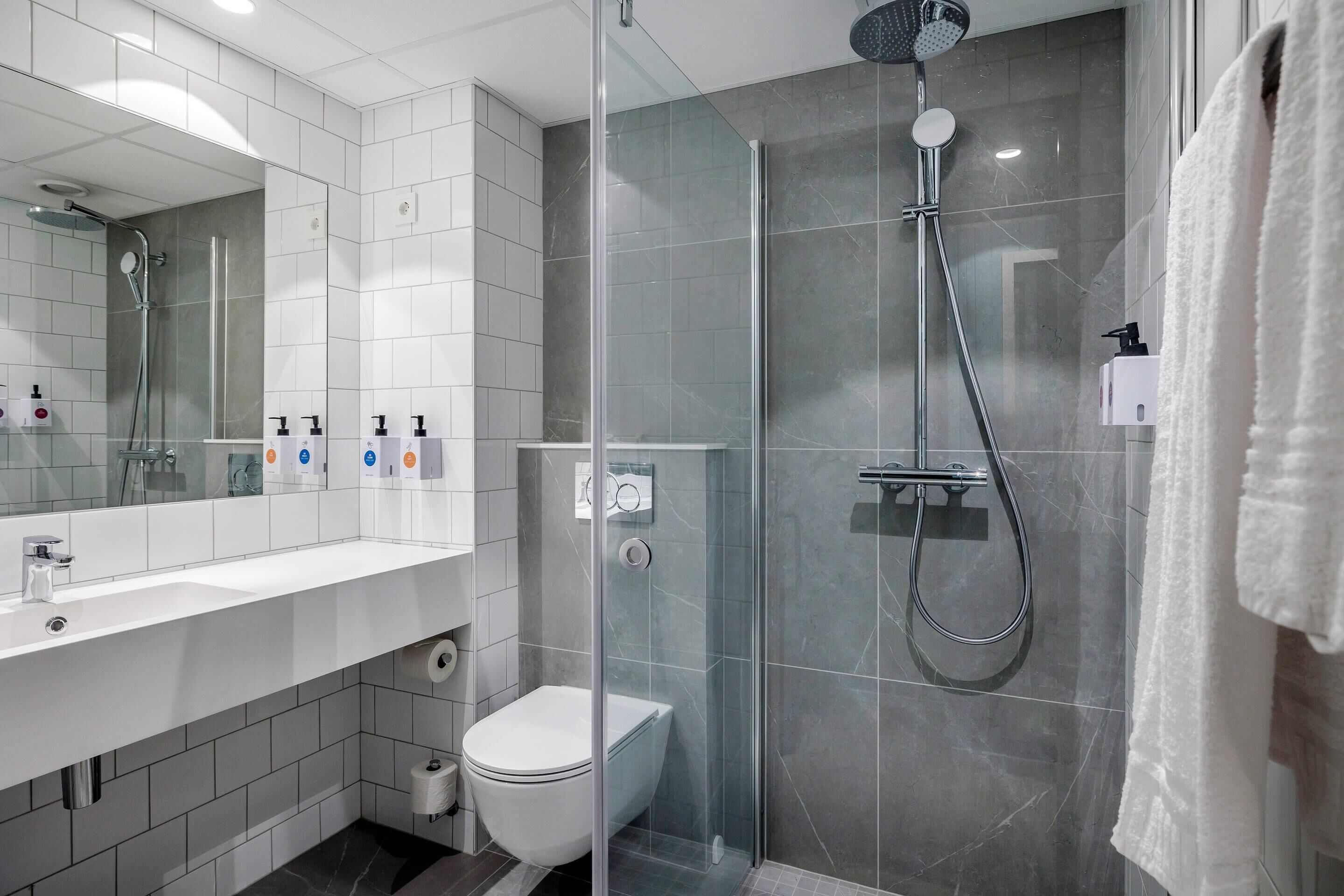 A modern bathroom with a glass-enclosed shower, a toilet, and a sink with soap dispensers.