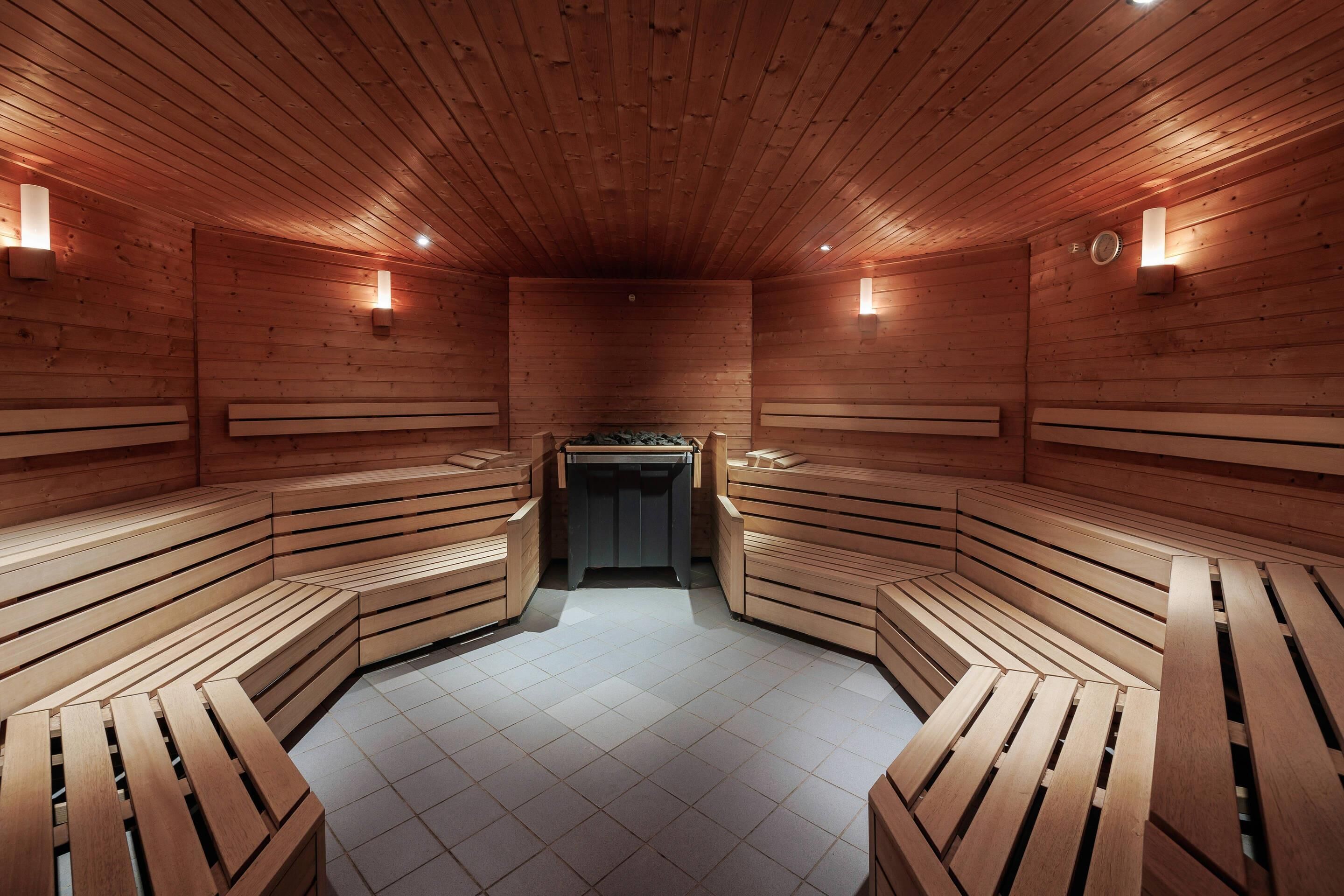 A sauna with wooden benches arranged in a semi-circular pattern, a tiled floor, and wall-mounted light fixtures.
