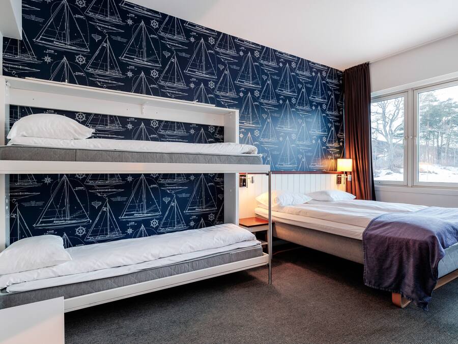 Et hotelværelse med køjesenge, et vindue med udsigt til træer og en væg med motiver af sejlbåde.