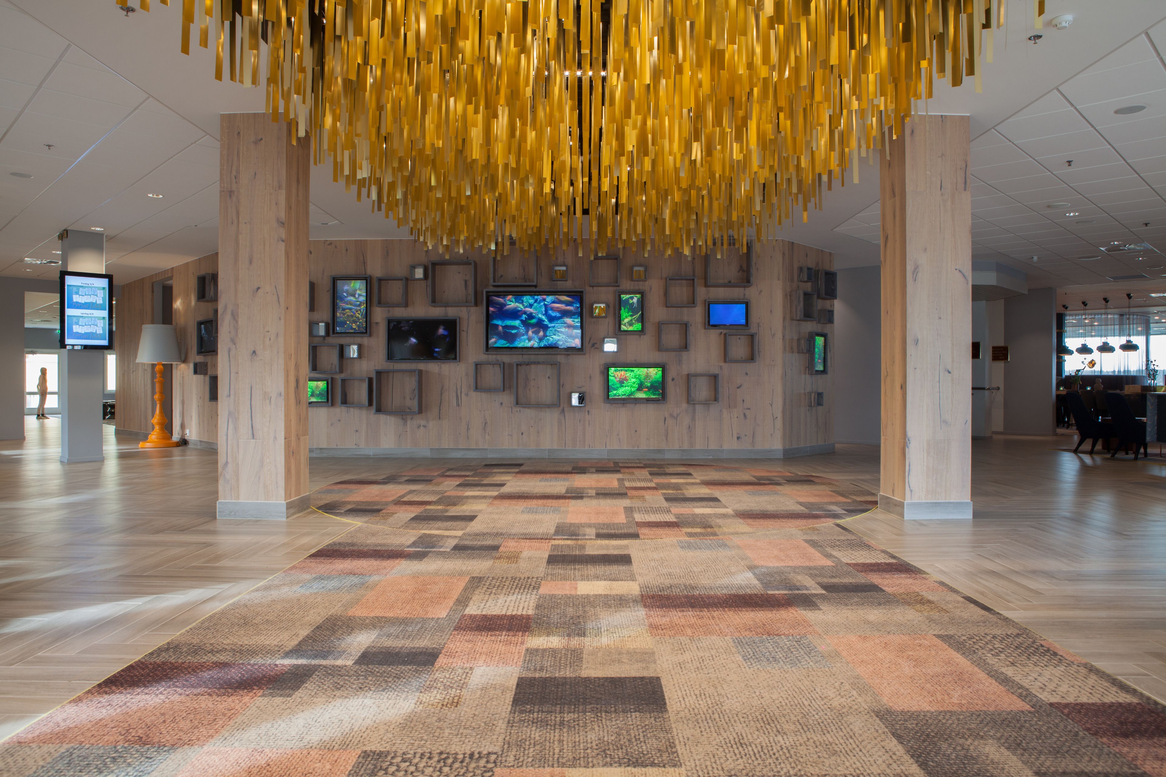 A spacious lobby with a patterned carpet, wooden walls, and multiple screens displaying content.