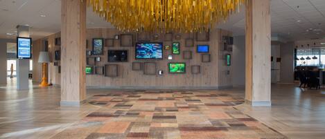 A spacious lobby with a patterned carpet, wooden walls, and multiple screens displaying content.