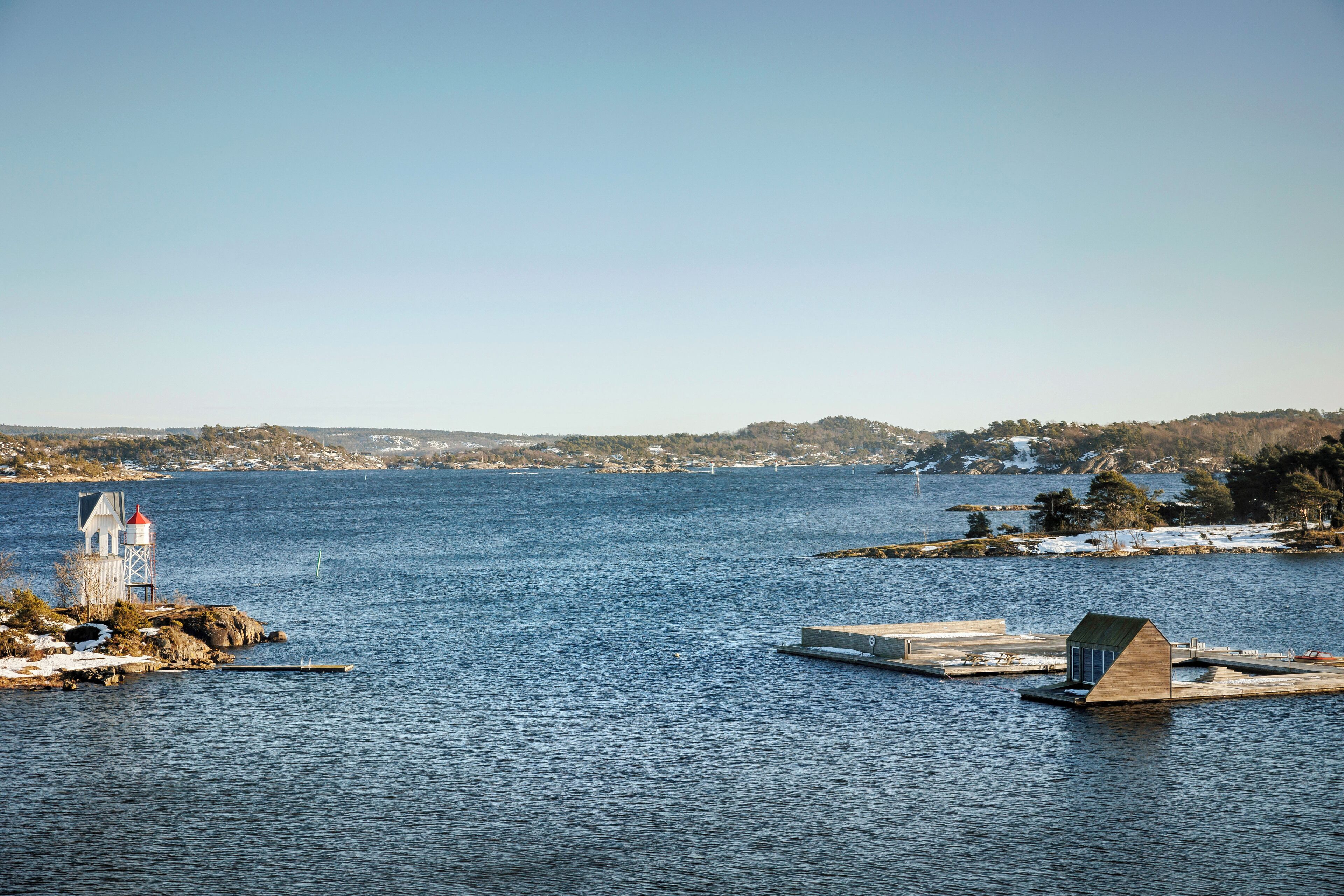 A lighthouse on a rocky shore with a clear view of the water and distant land.