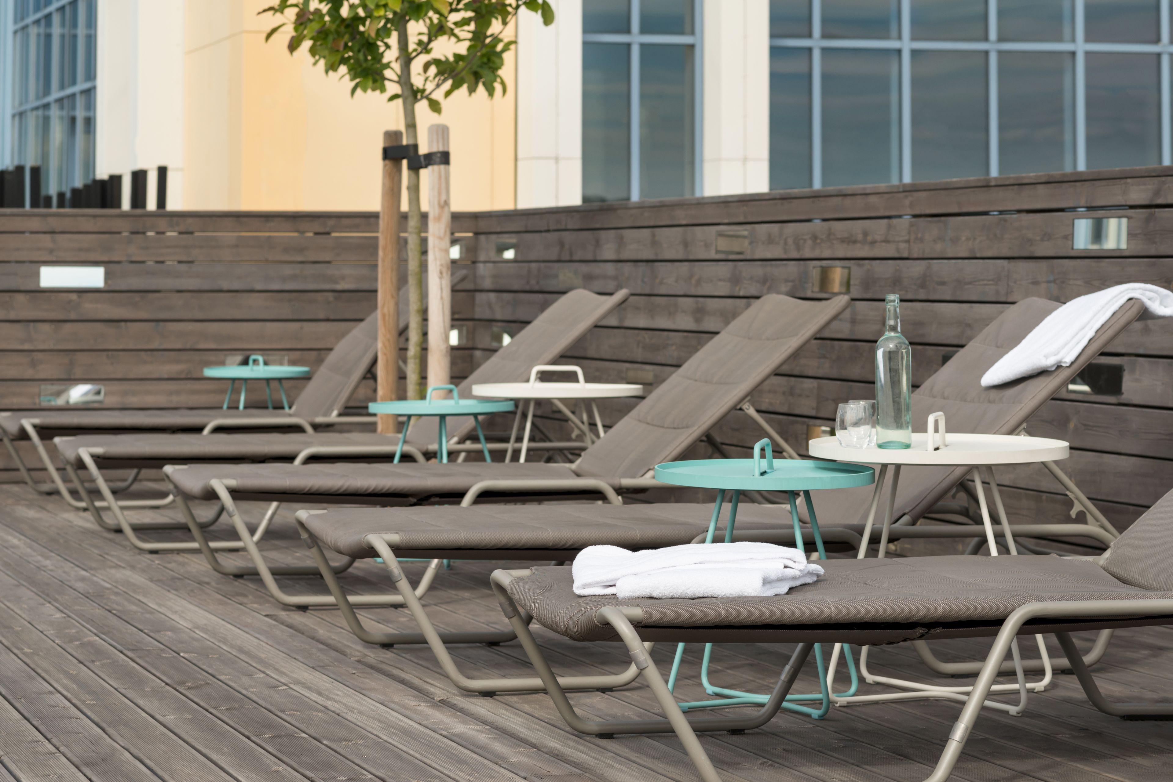 A row of sun loungers with towels, small tables, and a bottle of water.