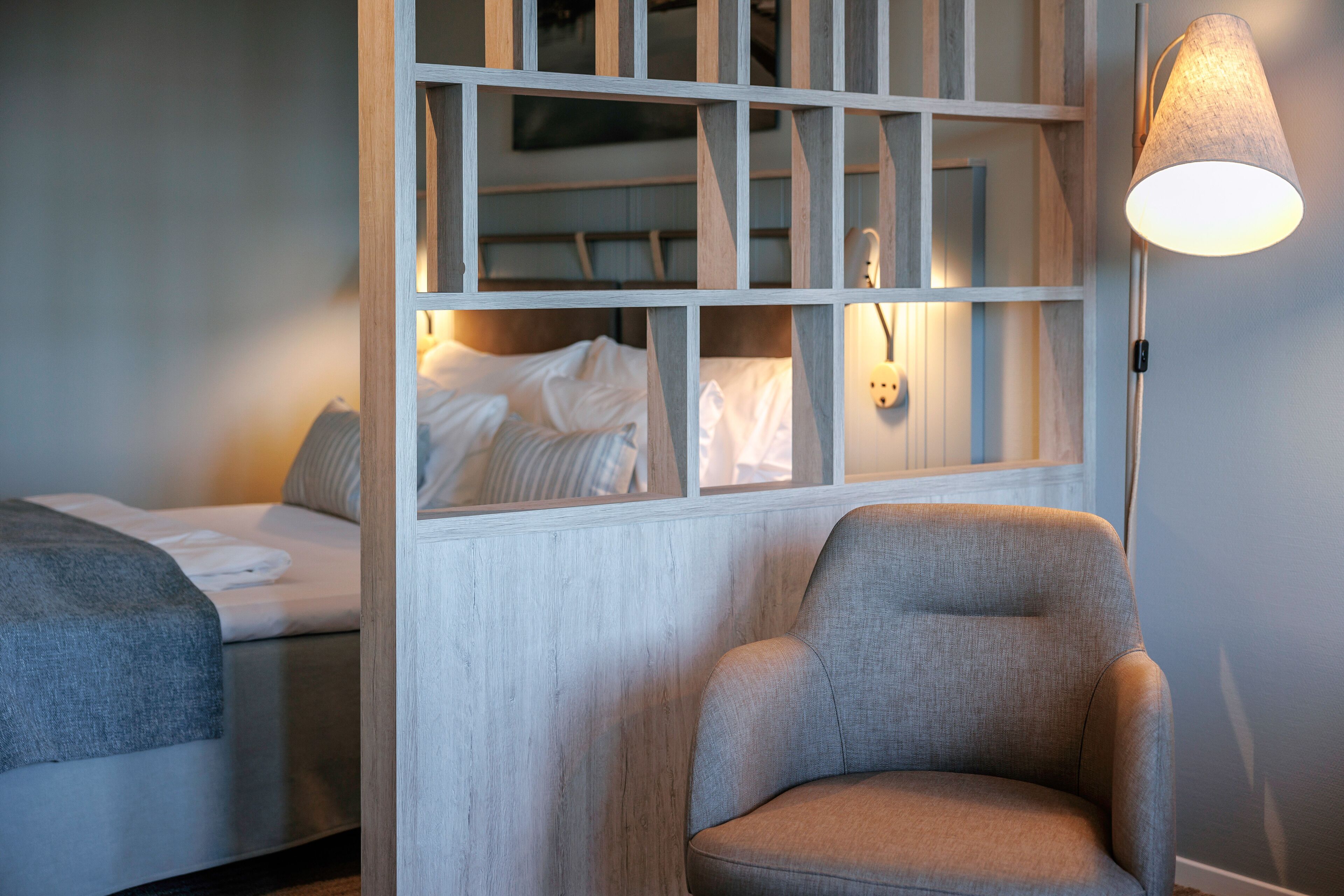A hotel room with a bed, a chair, and a lamp.