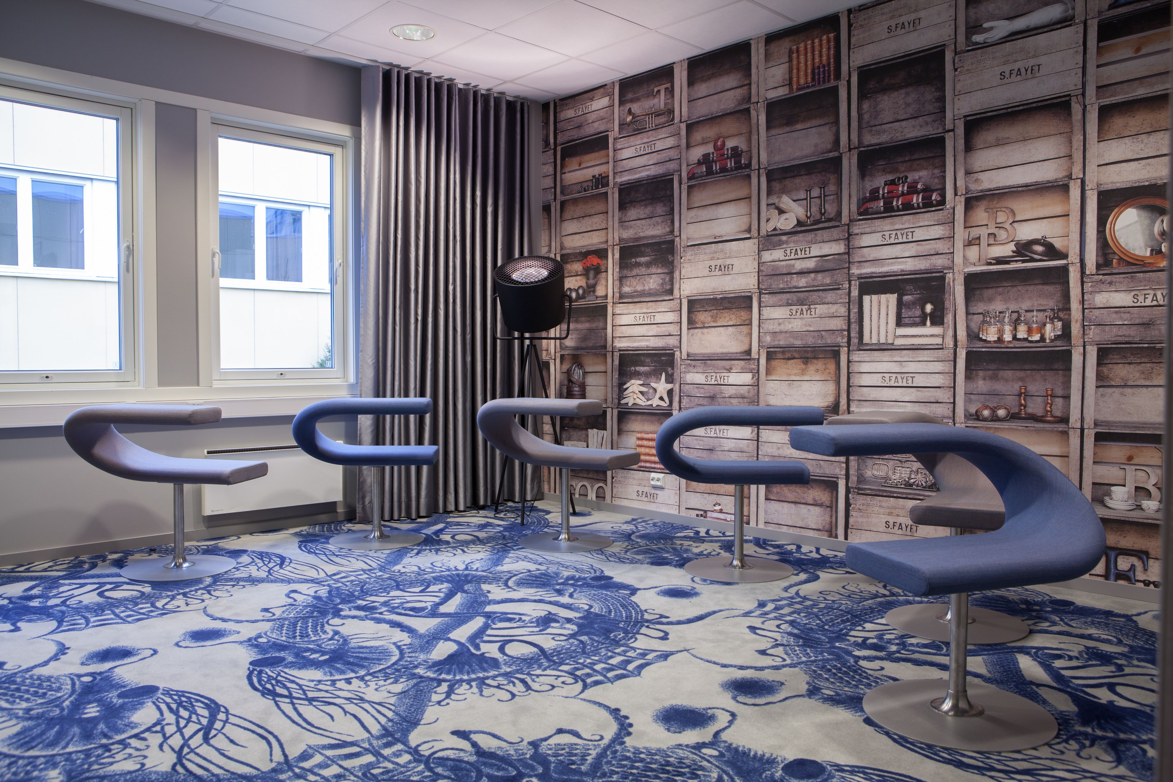 A room with a patterned carpet, three modern bar stools, a wall-mounted lamp, and a shelf with various items.