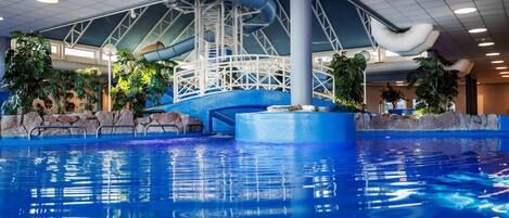 An indoor swimming pool with a water slide and a rock-lined pool edge.