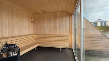 A sauna with wooden walls and benches, a black floor, and a window with a view of buildings outside.