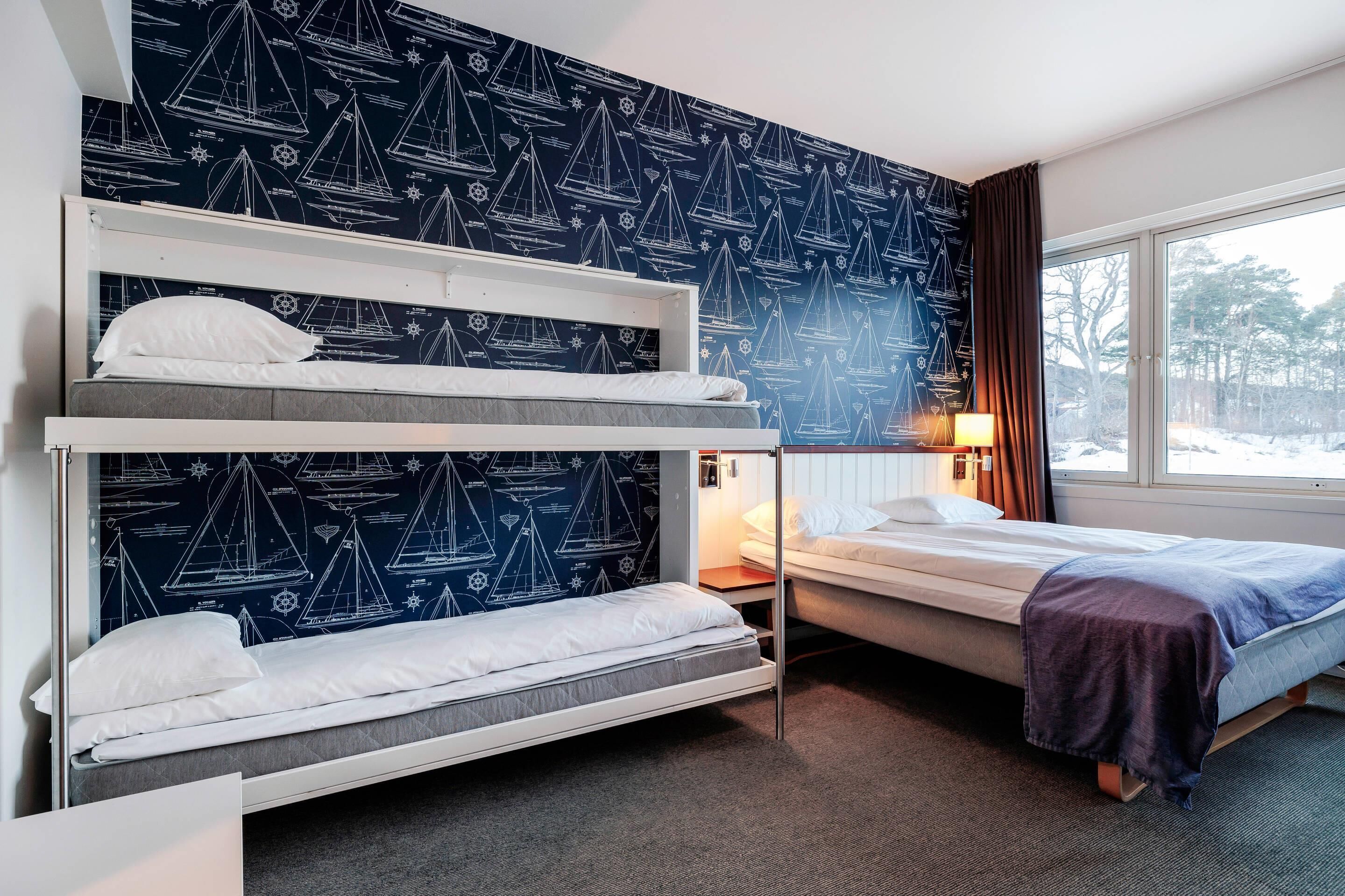 A hotel room with bunk beds, a window with a view of trees, and a wall with nautical-themed wallpaper.