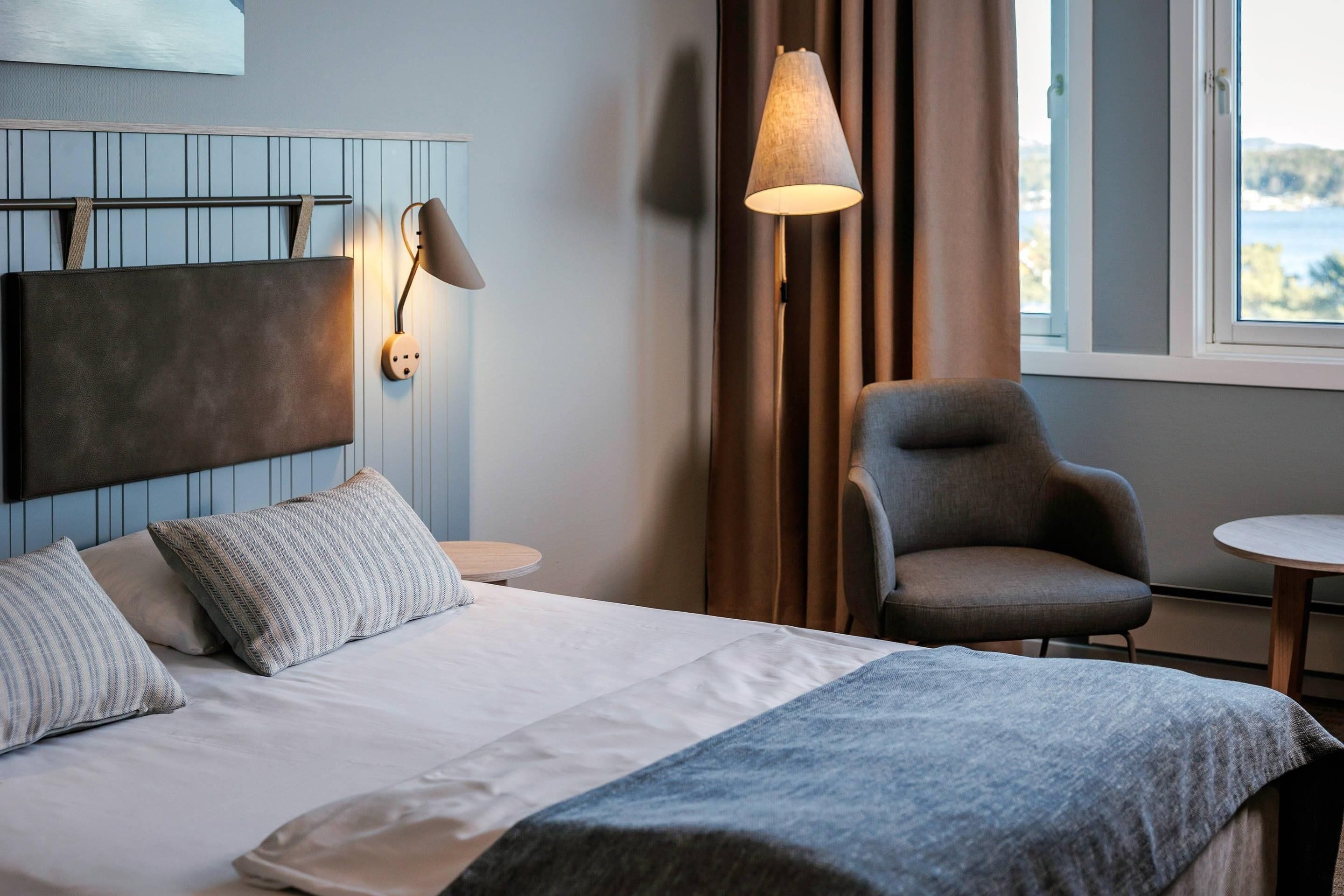 Una habitación de hotel con una cama, una silla, una lámpara y una ventana.