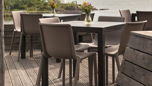 An outdoor deck with a table and chairs, overlooking a lake and a distant building. - Quality Hotel Skjaergarden (Bamble)