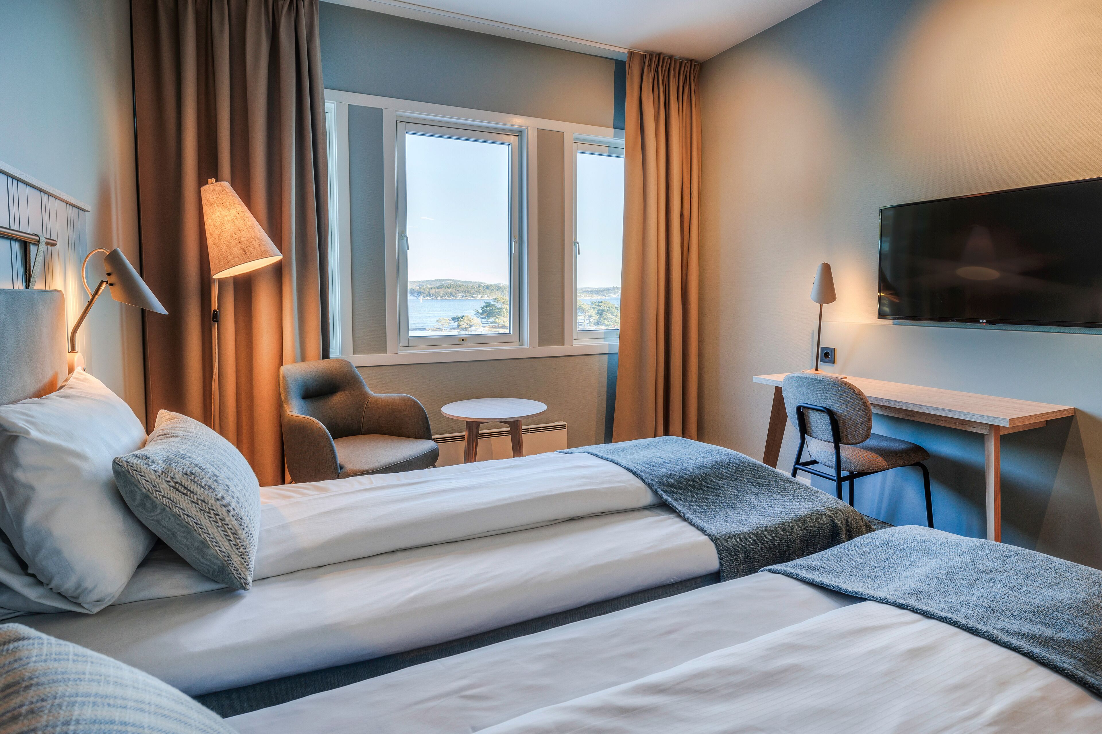 A hotel room with two beds, a desk, a chair, a TV, and a window with curtains.