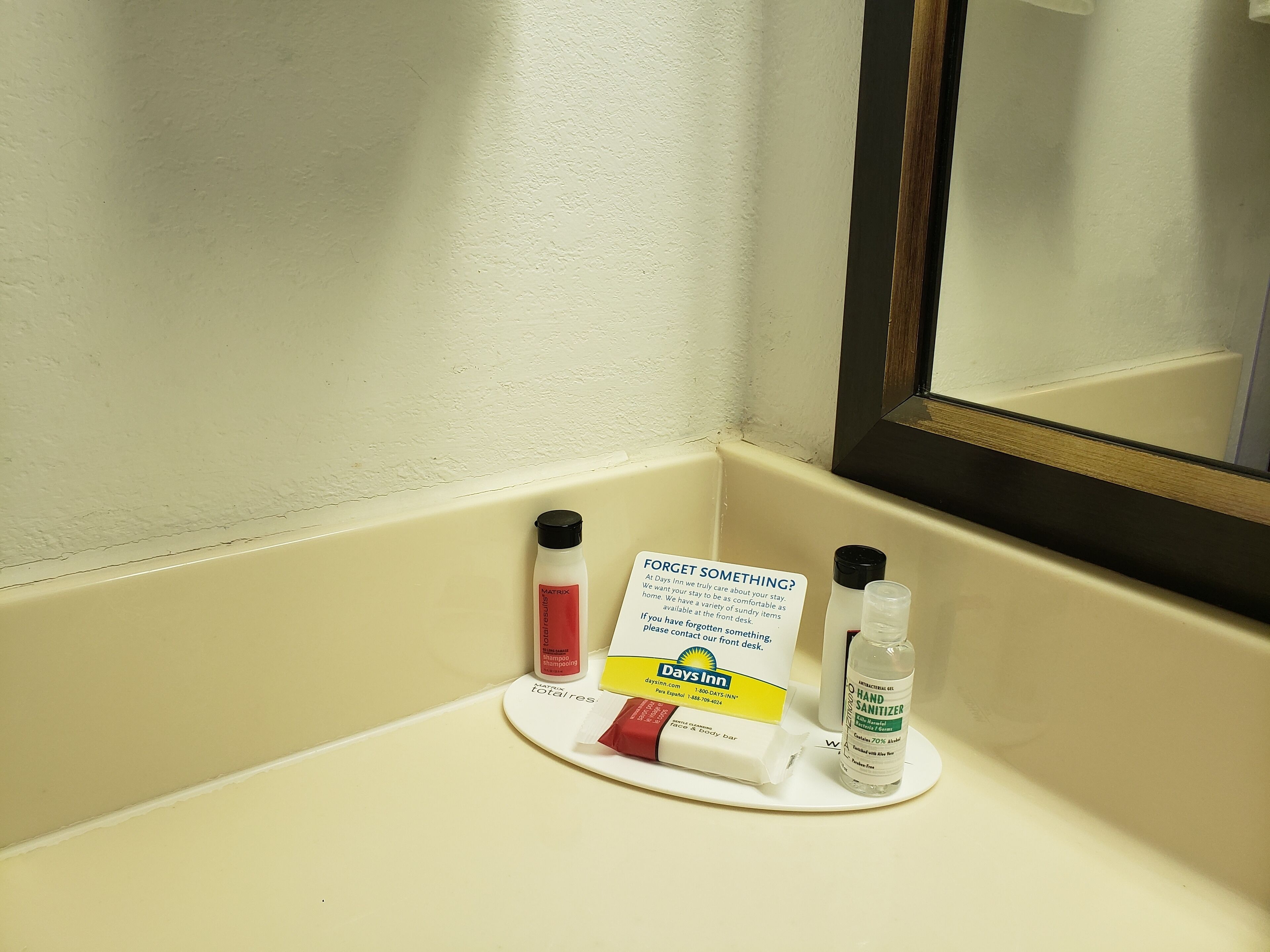 Un ripiano del bagno con articoli da toilette, tra cui shampoo, disinfettante per le mani e un avviso in caso di oggetti dimenticati.