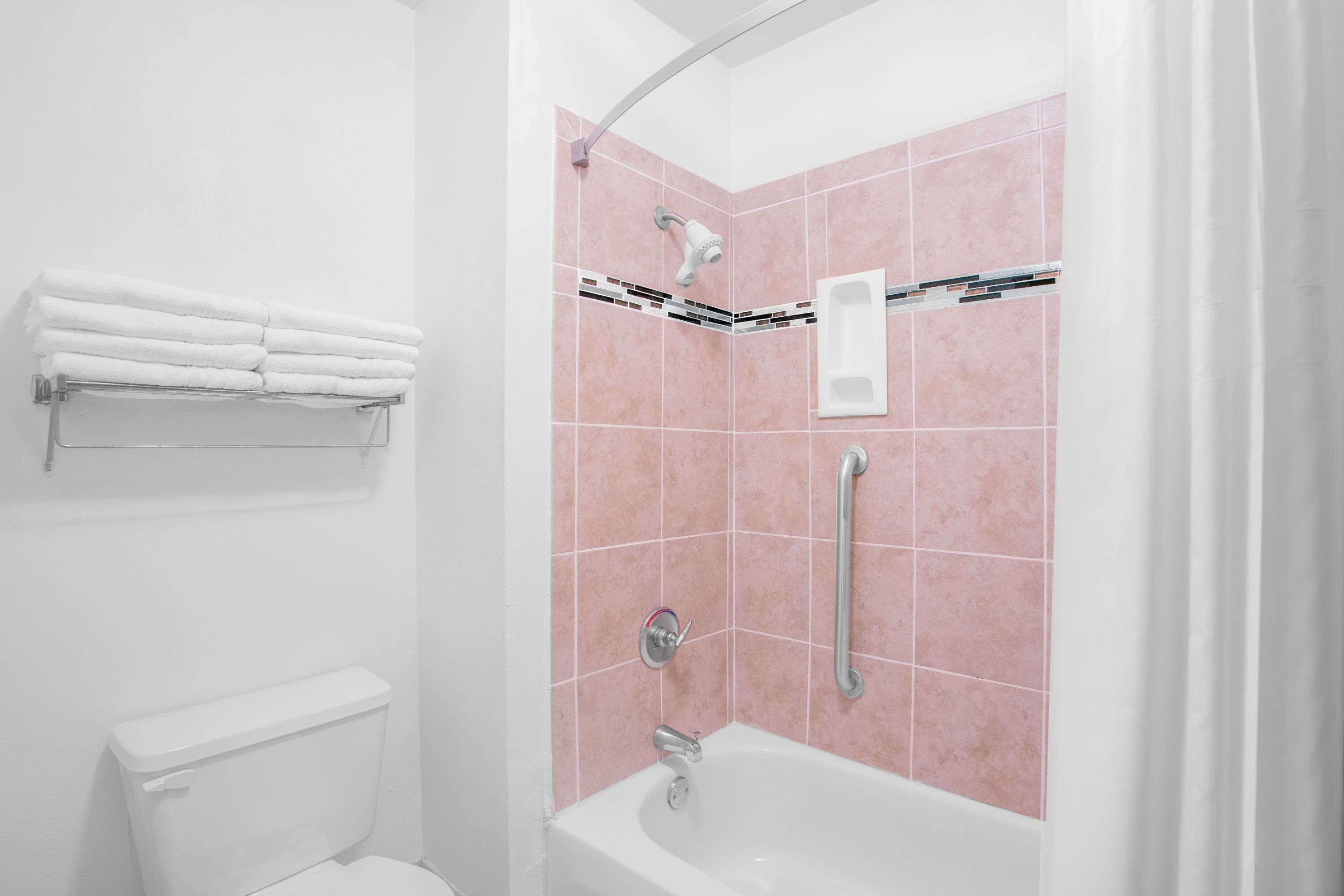 A bathroom with a white toilet, a white sink, a shower with pink tiles, and a towel rack with folded towels.