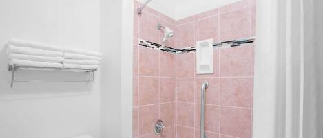 A bathroom with a white toilet, a white sink, a shower with pink tiles, and a towel rack with folded towels.