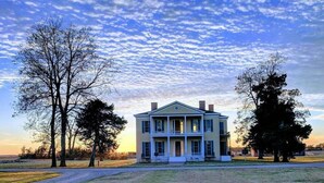 A large, two-story house with a front porch, surrounded by a grassy field and trees. - Days Inn by Wyndham Lake Village (Lake Village)