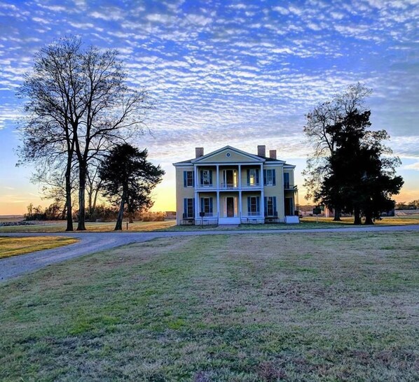 A large, two-story house with a front porch, surrounded by a grassy field and trees. - Days Inn by Wyndham Lake Village (Lake Village)