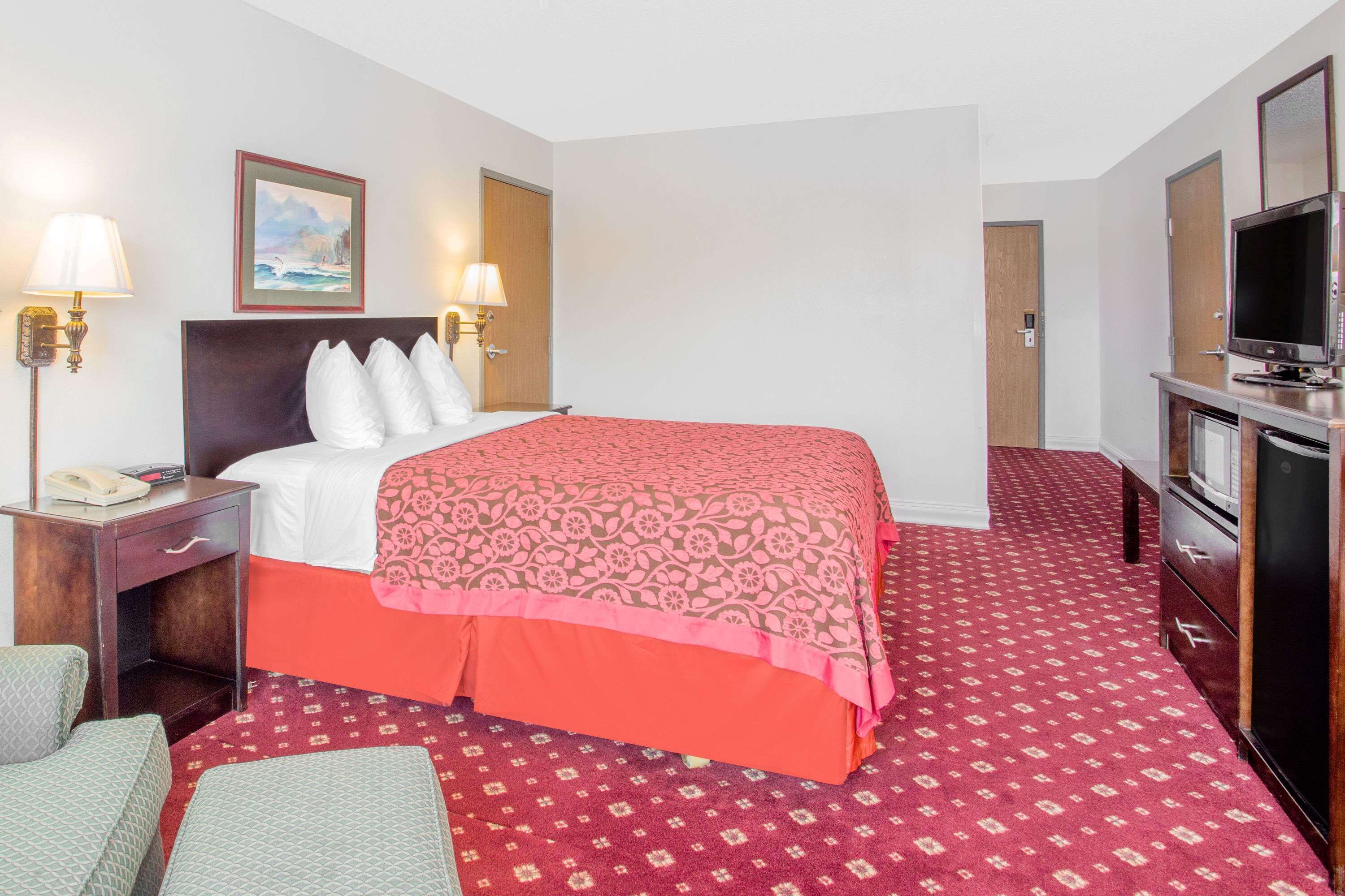 A hotel room with a bed, two bedside lamps, a television, a desk with a telephone, and a door.