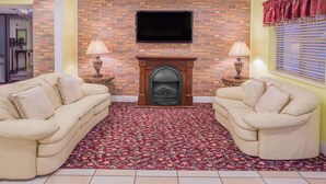 A living room with two beige sofas, a fireplace, and a flat-screen TV mounted on a brick wall. - Days Inn by Wyndham Lake Village (Lake Village)