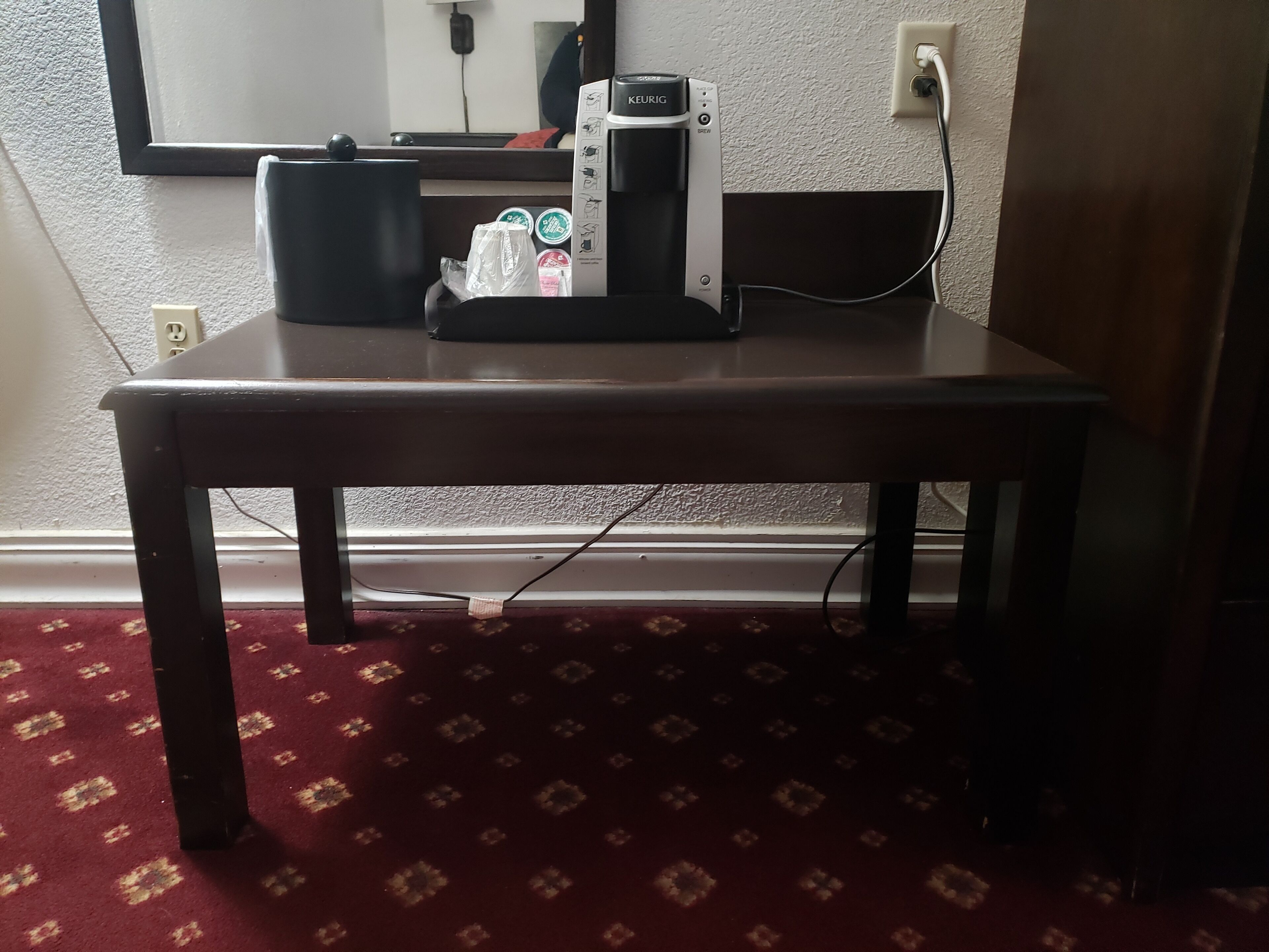 A small table with a coffee maker, a bag, and a water bottle.