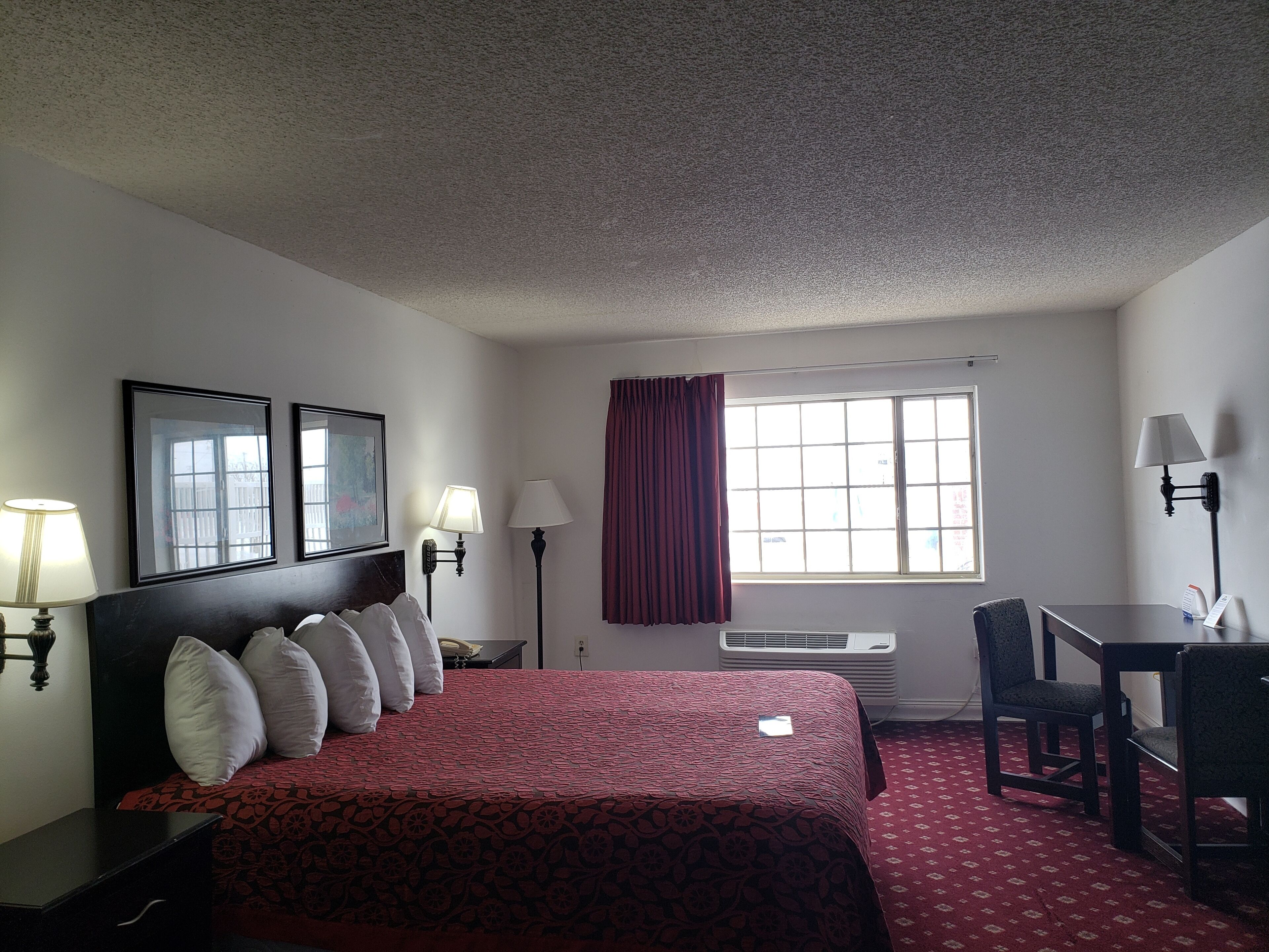 Habitación de hotel con cama, dos lámparas de noche, escritorio con silla, ventana con cortinas y aire acondicionado.
