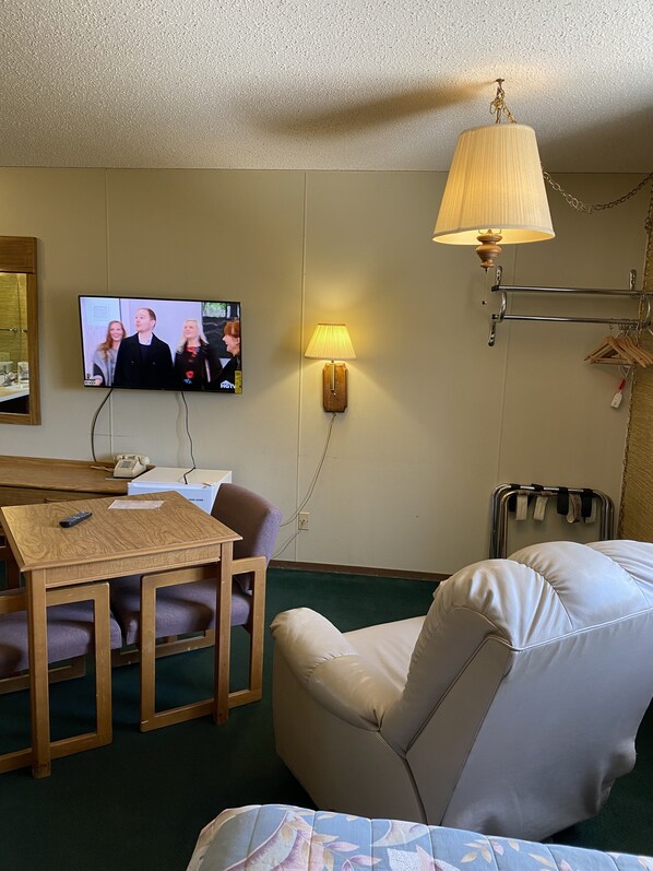 A hotel room with a television, a table with chairs, a lamp, and a bed. - Burr Oak Motel (Algona)