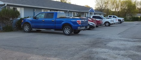Un estacionamiento con varios vehículos, incluyendo una camioneta azul y un SUV blanco.