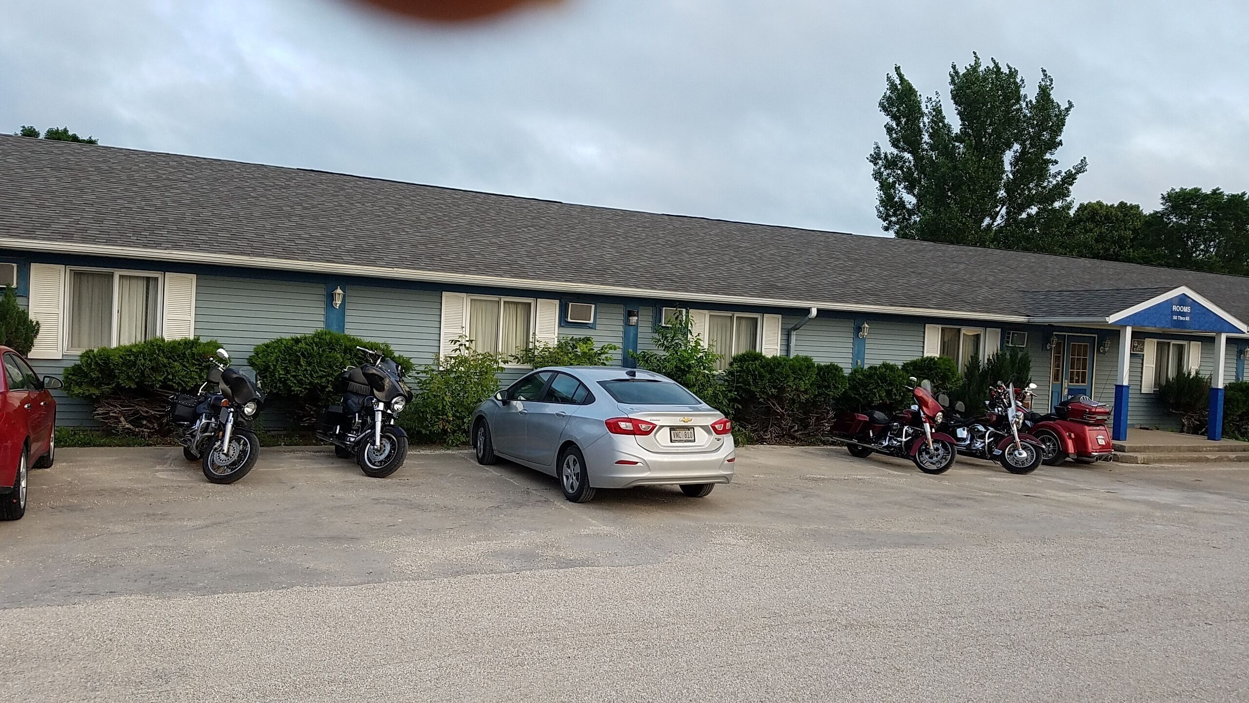 A motel with a parking lot, several motorcycles, and a silver sedan.