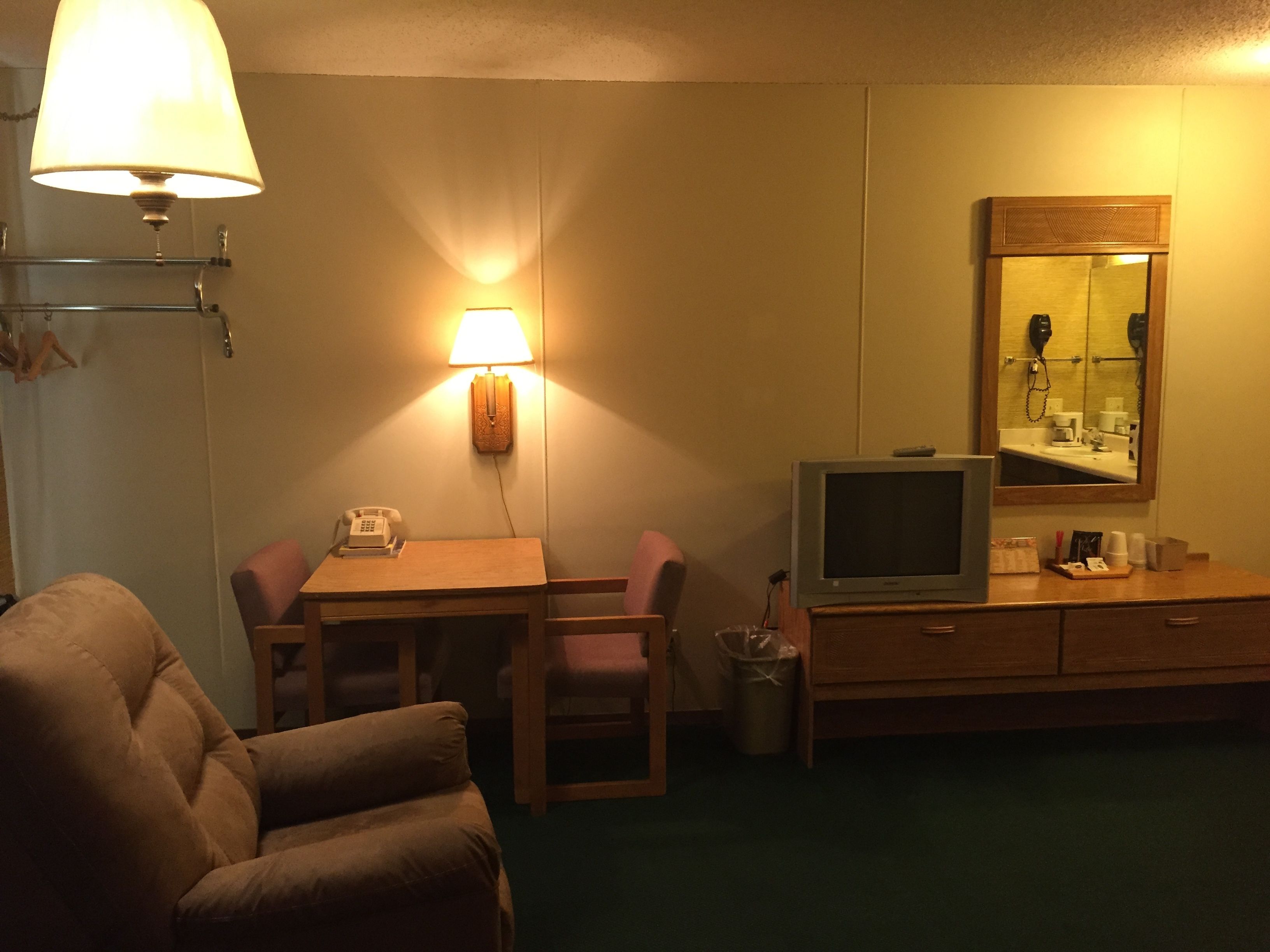A hotel room with a bed, a desk with a lamp, a television, a mirror, and a trash can.