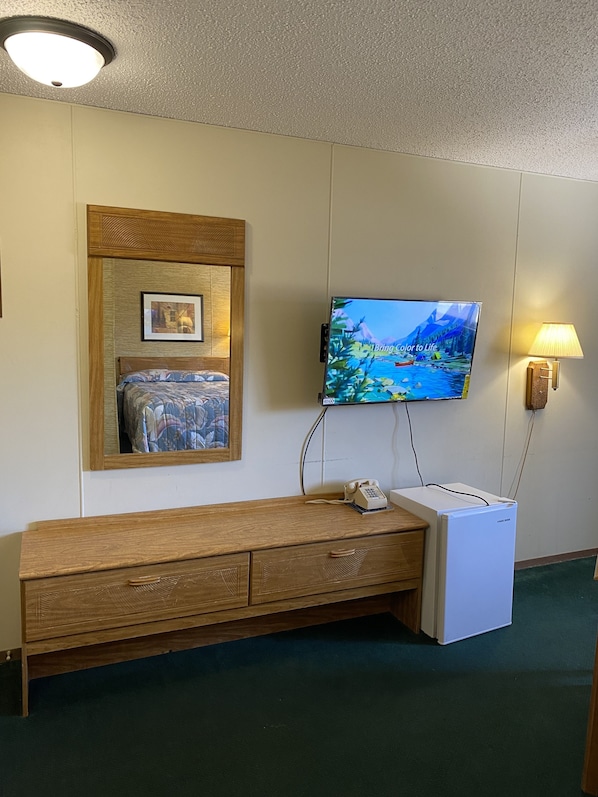 A hotel room with a wooden bench, a television mounted on the wall, a framed picture above the bench, and a wall-mounted telephone. - Burr Oak Motel (Algona)