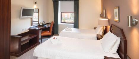 A hotel room with two beds, a desk, a chair, a TV, and a window with curtains.