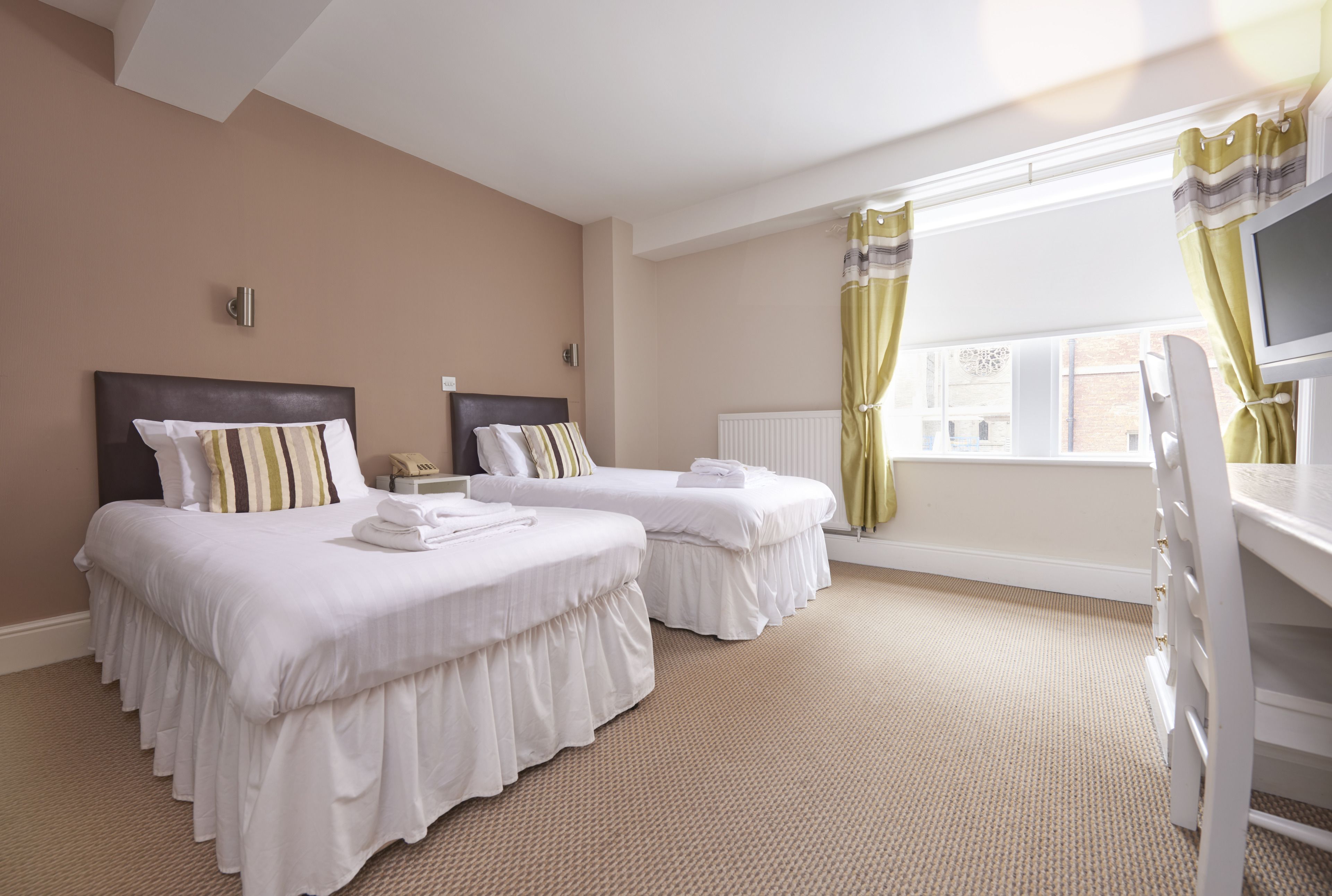 Habitación de hotel con dos camas, televisión, ventana con cortinas y radiador.
