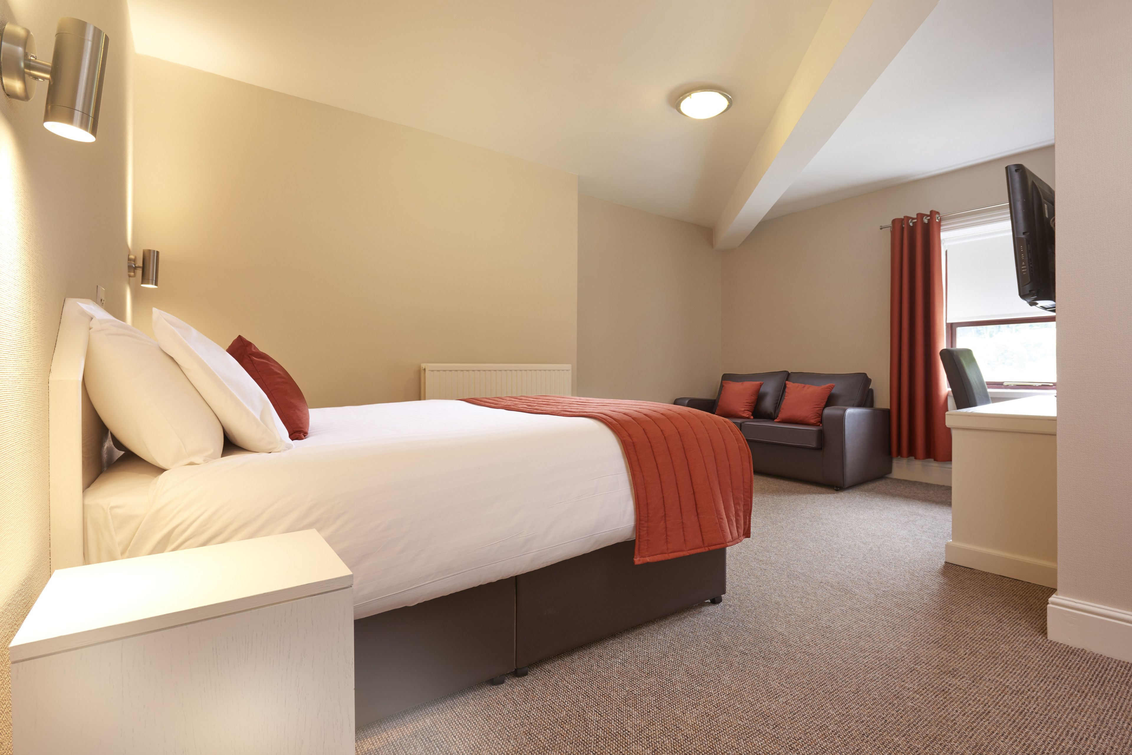 Une chambre d’hôtel moderne avec un grand lit, un canapé, une télévision et une fenêtre avec des rideaux.