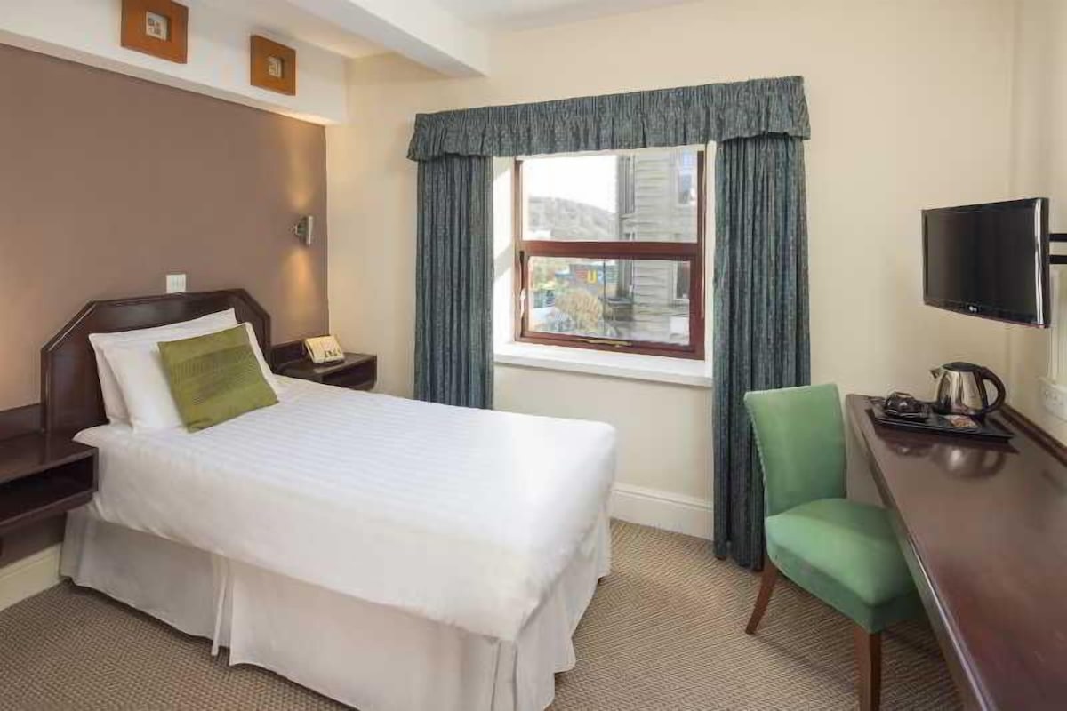 A hotel room with a bed, a desk, a chair, a television, and a window with curtains.