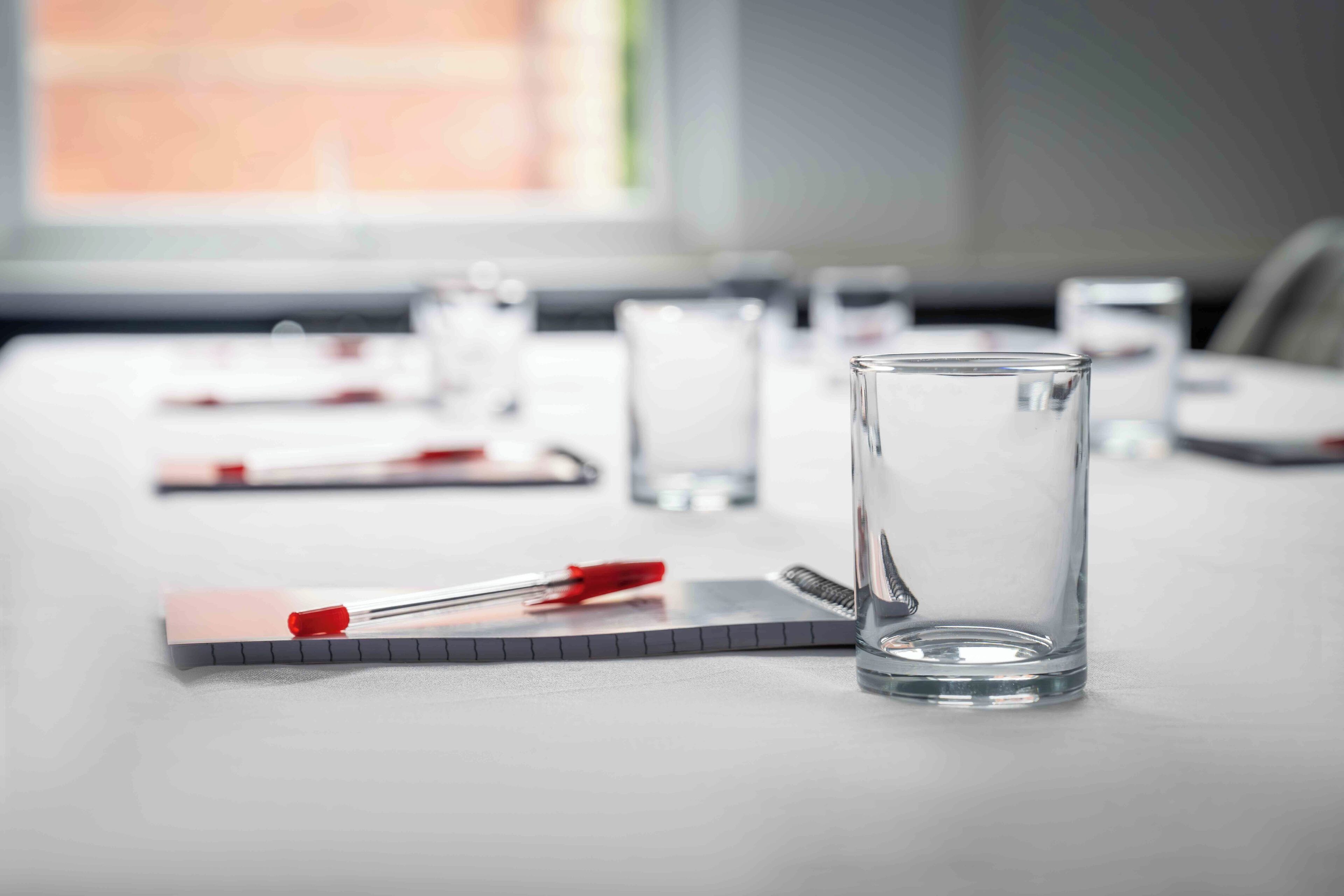 A conference table with a glass of water, a notepad, and a red pen.