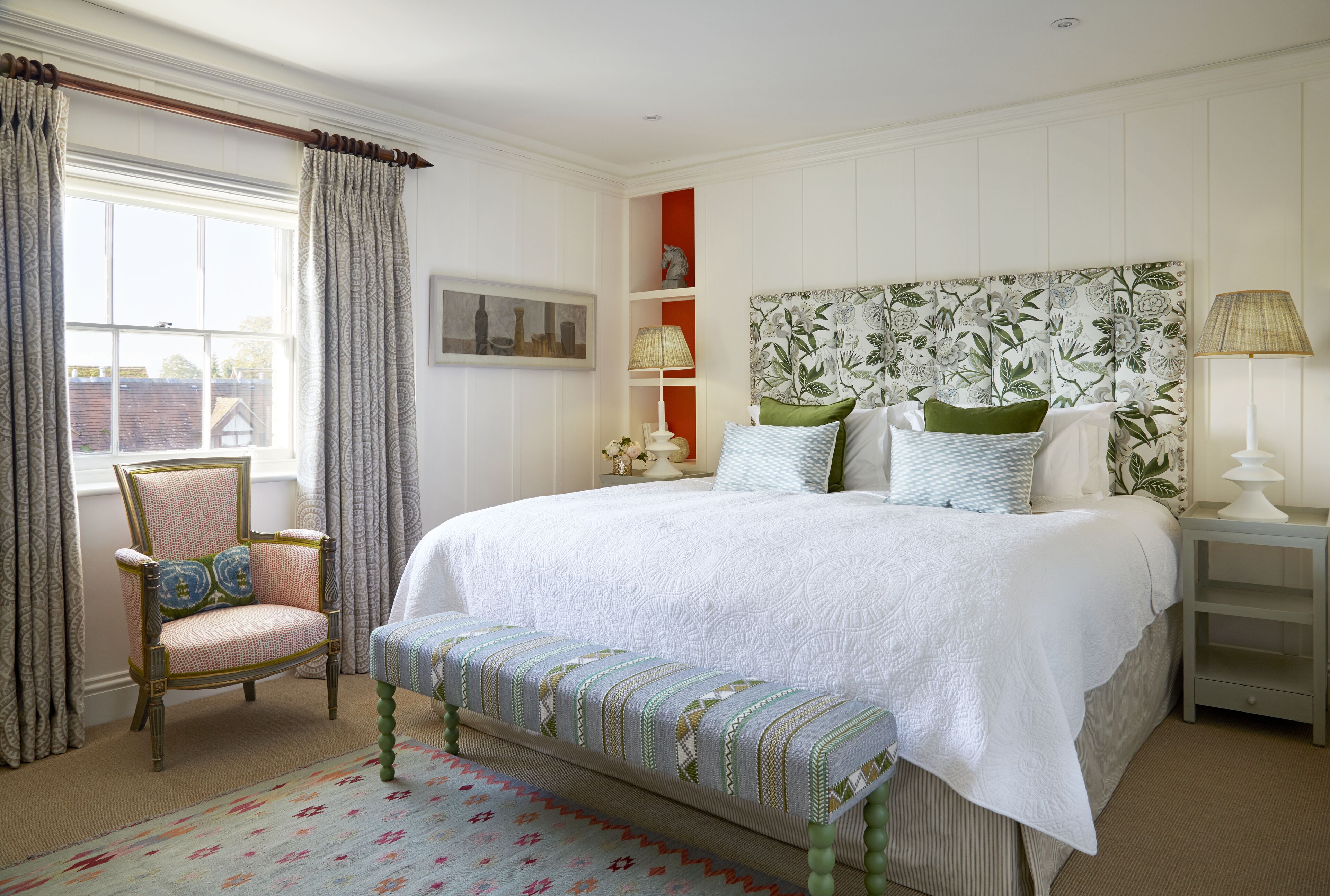 Une chambre à coucher avec un grand lit, une chaise, un banc et une table de chevet.