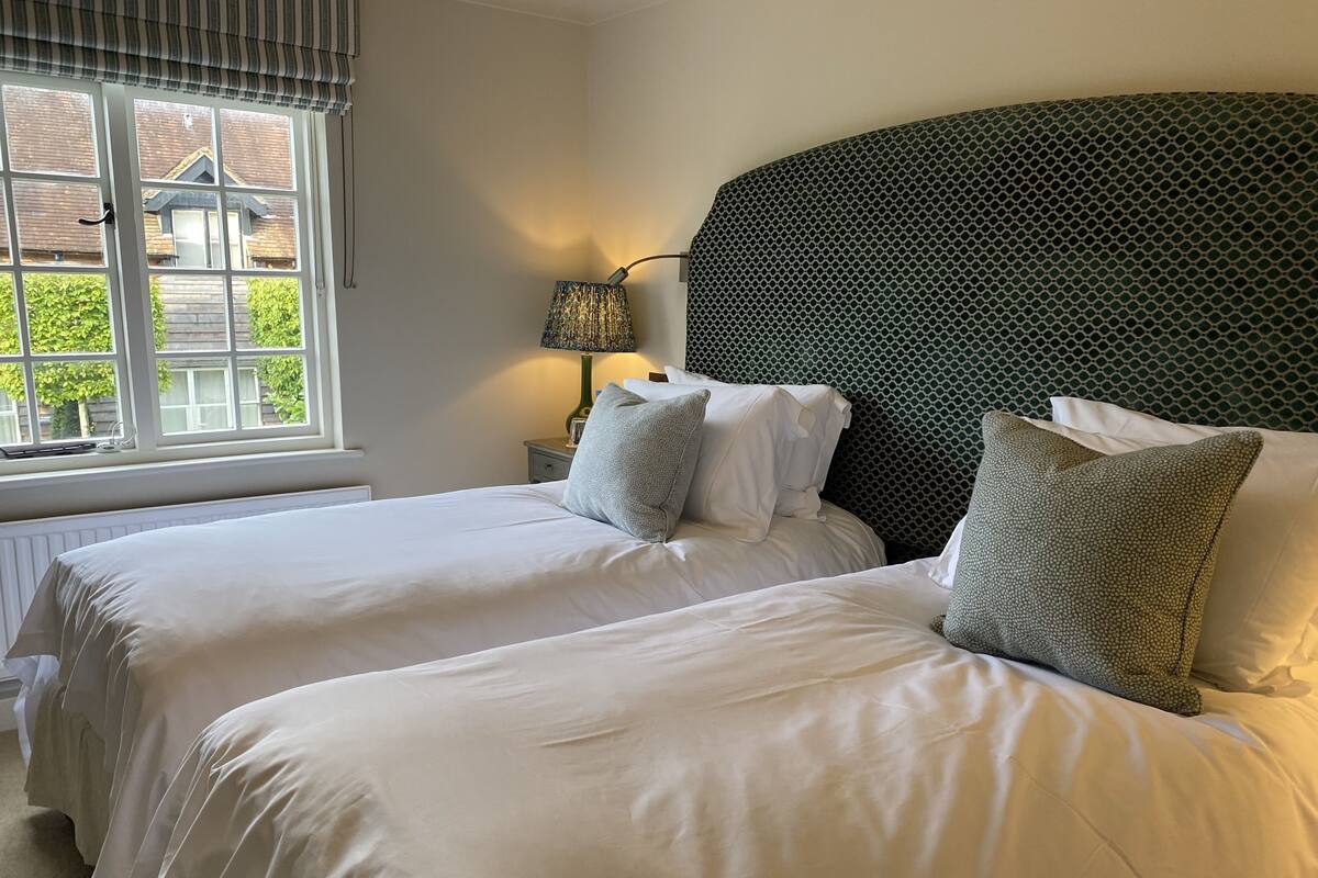 A hotel room with two beds, a window with blinds, a lamp, and a patterned headboard.