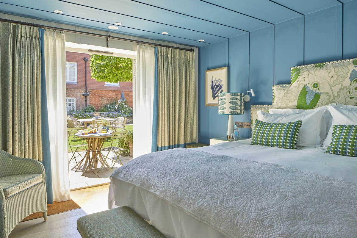 A bedroom with a large bed, a bench, a table, and chairs outside the window.