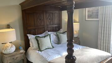 A four-poster bed with a wooden headboard, white bedding, and decorative pillows. There are two bedside tables with lamps and a decorative vase.