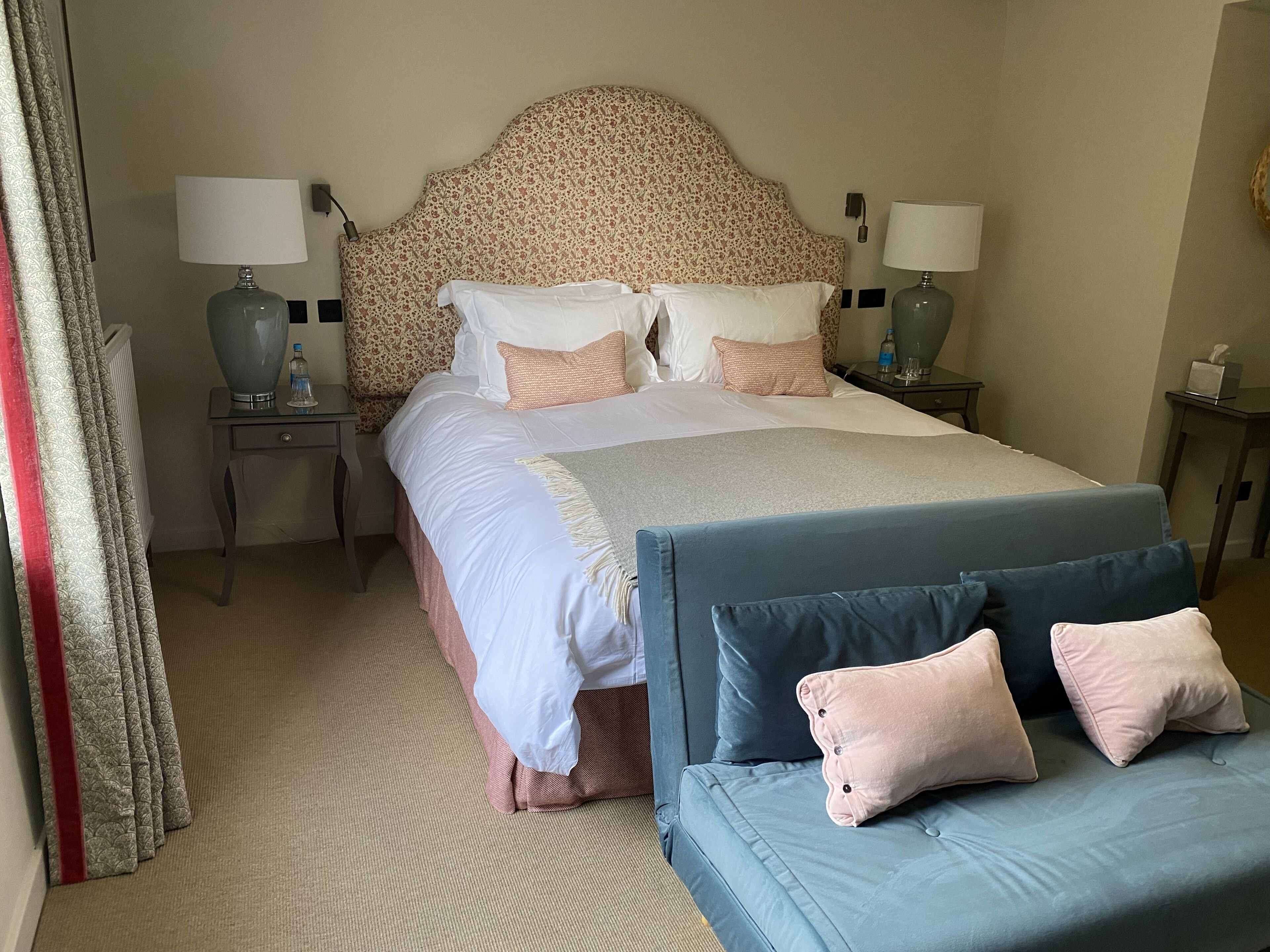 A hotel room with a bed, two bedside tables, a sofa, and a headboard.